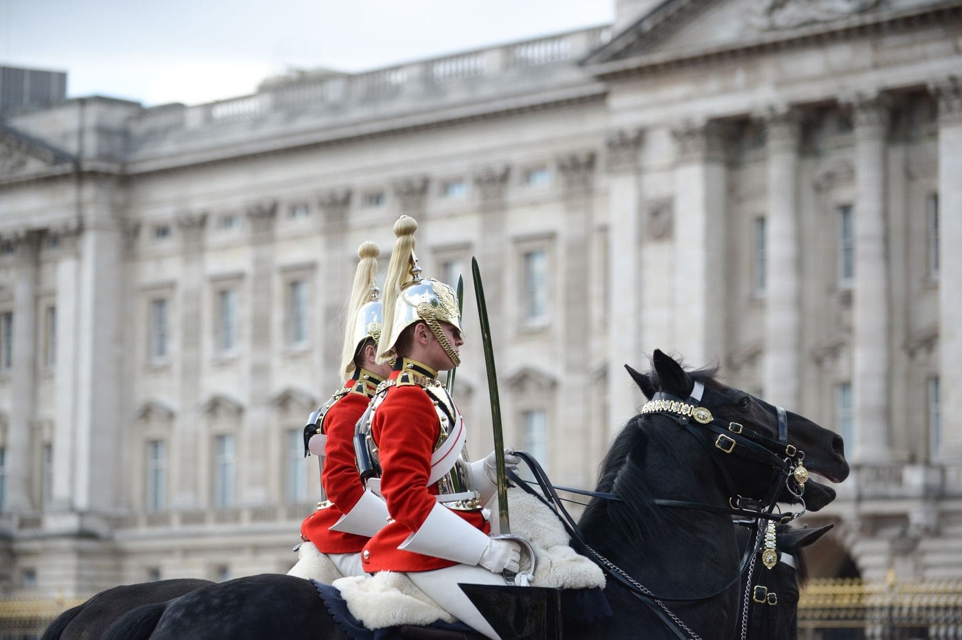 Zwei berittene Soldaten in roten Zeremonialuniformen und silbernen Helmen paradieren vor der imposanten Steinfassade der Horse Guards Parade in London.