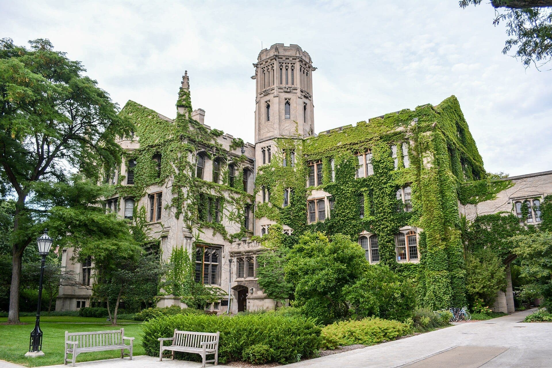 Gothic-style university building in Hyde Park, Chicago, covered in ivy with lush green trees, benches, and a pathway in front.