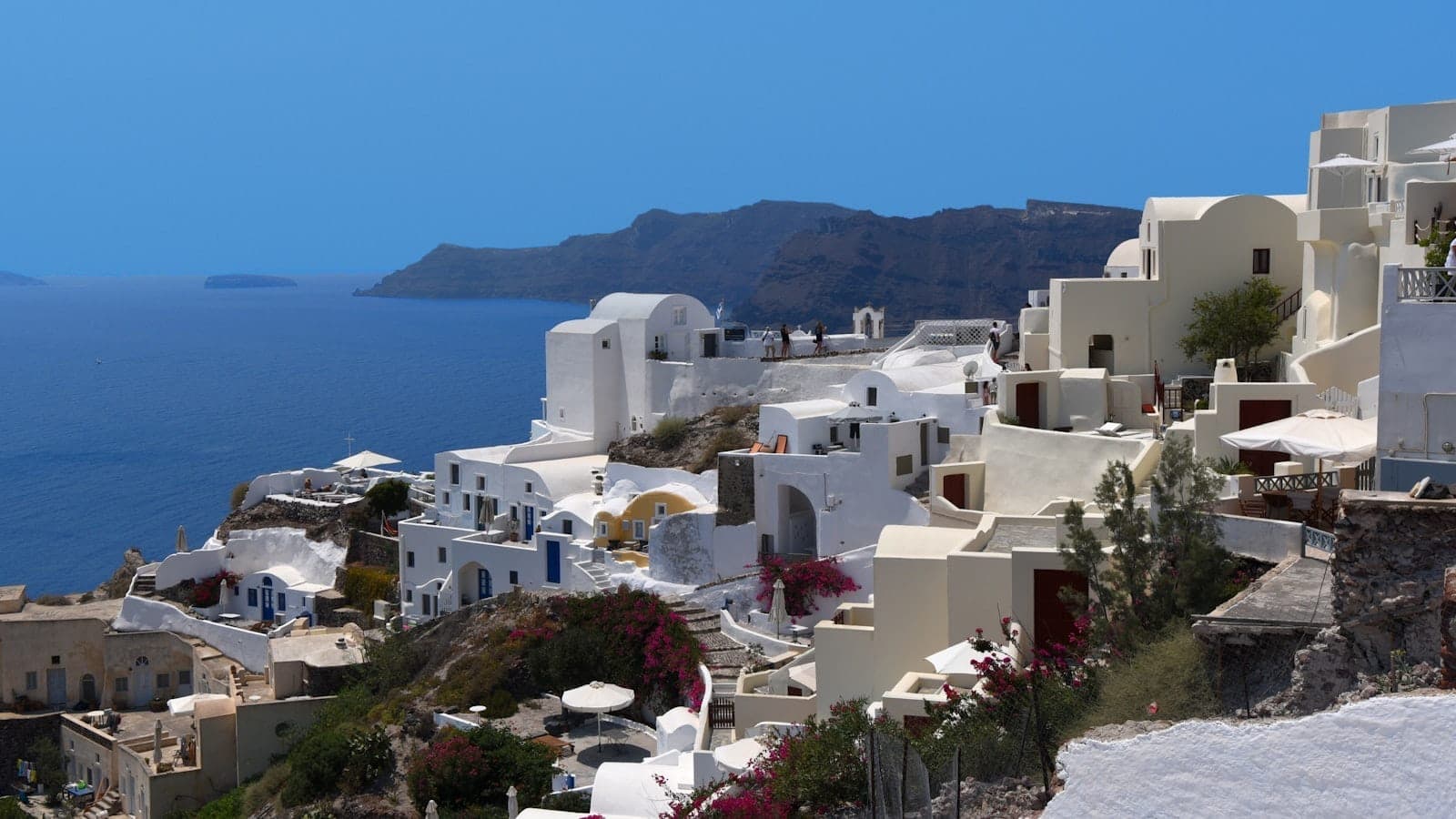 Klassische weiß getünchte Gebäude von Imerovigli am Rand der Kaldera, mit strahlendem blauem Himmel und dem Meer im Hintergrund.