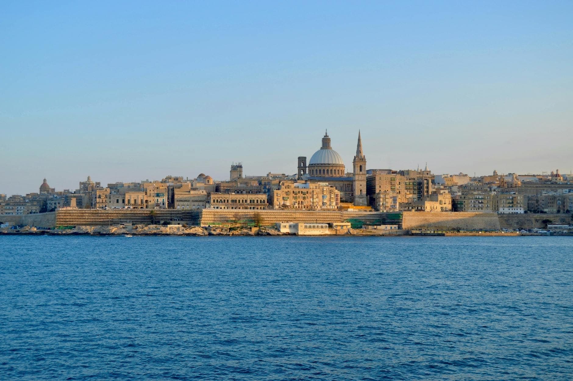 Blick auf die Skyline von Valletta mit historischen Kuppeln und Kirchtürmen, die über honigfarbenen Steingebäuden aufragen – bei Sonnenuntergang vom blauen Mittelmeer aus gesehen.