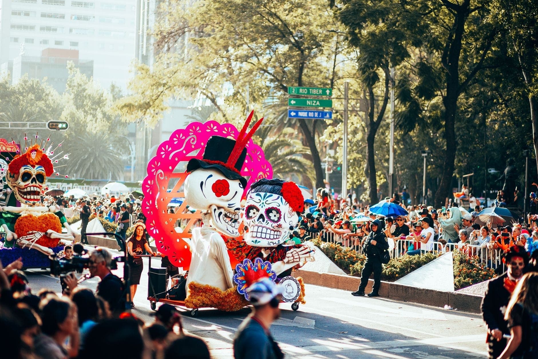 ขบวนพาเหรดตอนกลางวันในช่วง Día de Muertos ที่ Mexico City พร้อมรถแห่รูป calavera ขนาดใหญ่และฝูงชนหนาแน่นเรียงรายตามท้องถนน