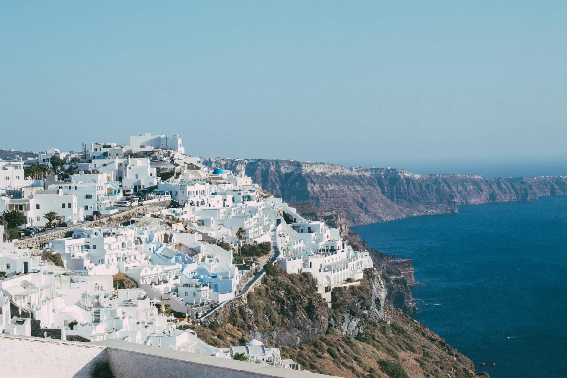 Weiße Gebäude von Santorini thronen auf Klippen mit Blick auf das tiefblaue Ägäische Meer und die dramatische Vulkankaldera.