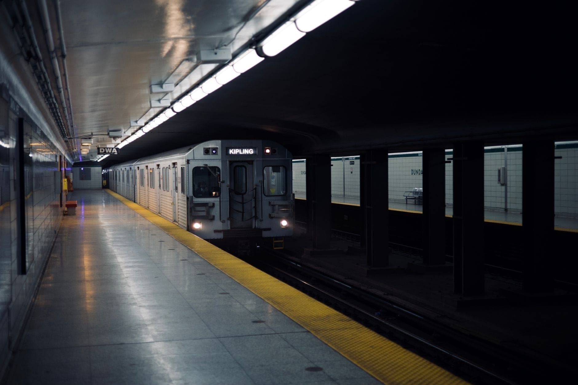 A TTC subway train arriving at an underground Toronto station with bright lighting and yellow safety line.
