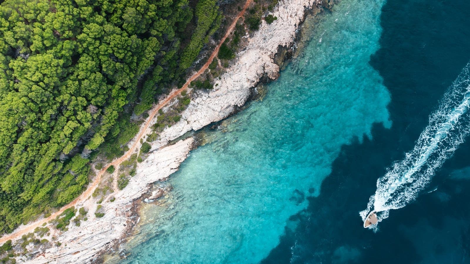 Vista aerea di uno speedboat che naviga lungo la costa turchese di una lussureggiante isola dalmata in Croazia.