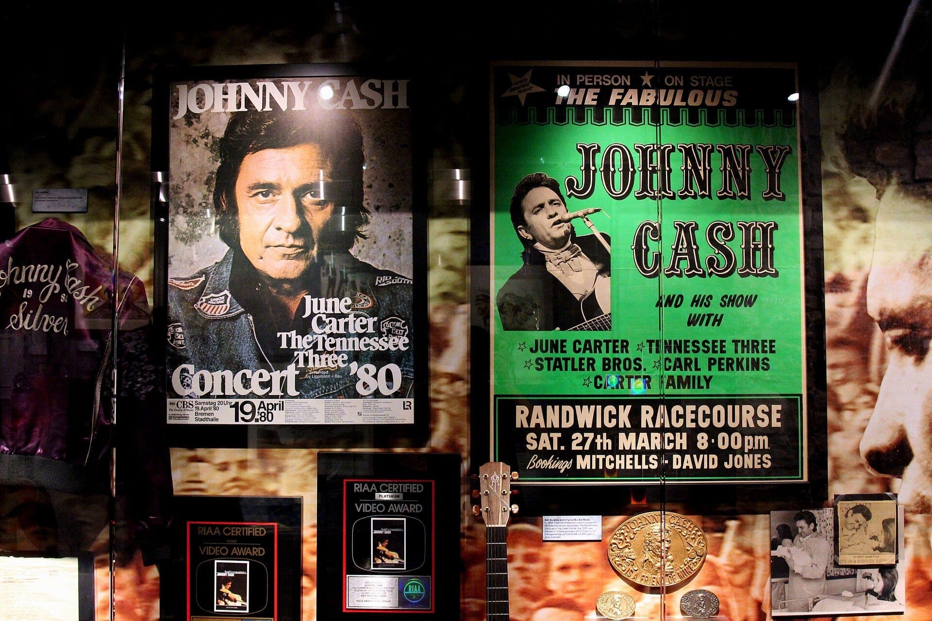 Johnny Cash Museum display featuring vintage concert posters, a purple tour jacket, and RIAA award plaques under glass in a dimly lit exhibit.