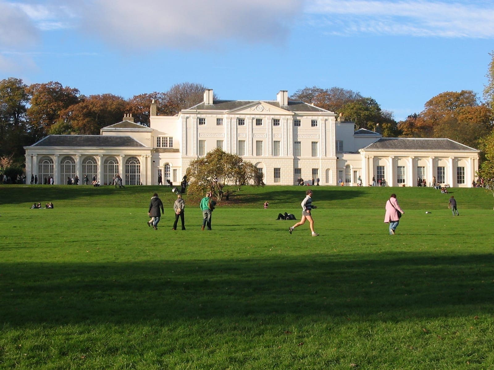 Das Kenwood House liegt unter einem blauen Himmel, umgeben von üppigen grünen Rasenflächen und Besuchern, die auf Hampstead Heath spazieren und entspannen.