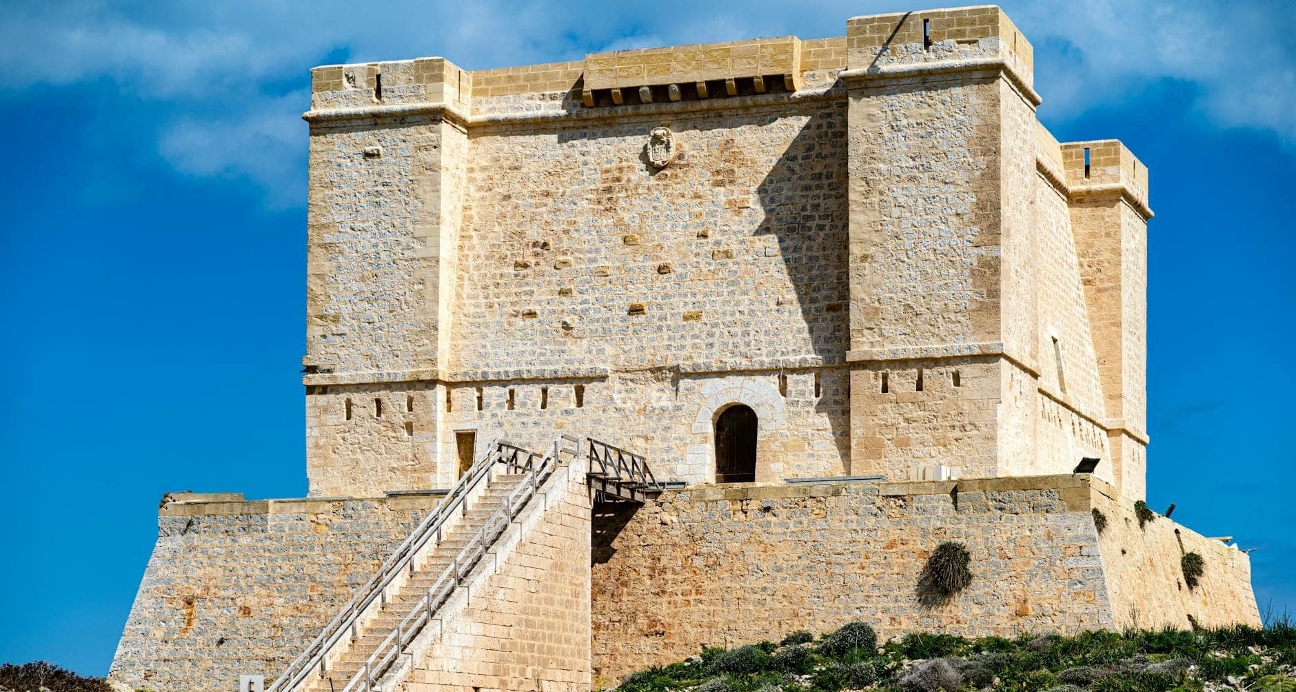 Imposante Steinfestung mit einer breiten Treppe, die zu einem Bogendurchgang führt, unter blauem Himmel auf Malta.