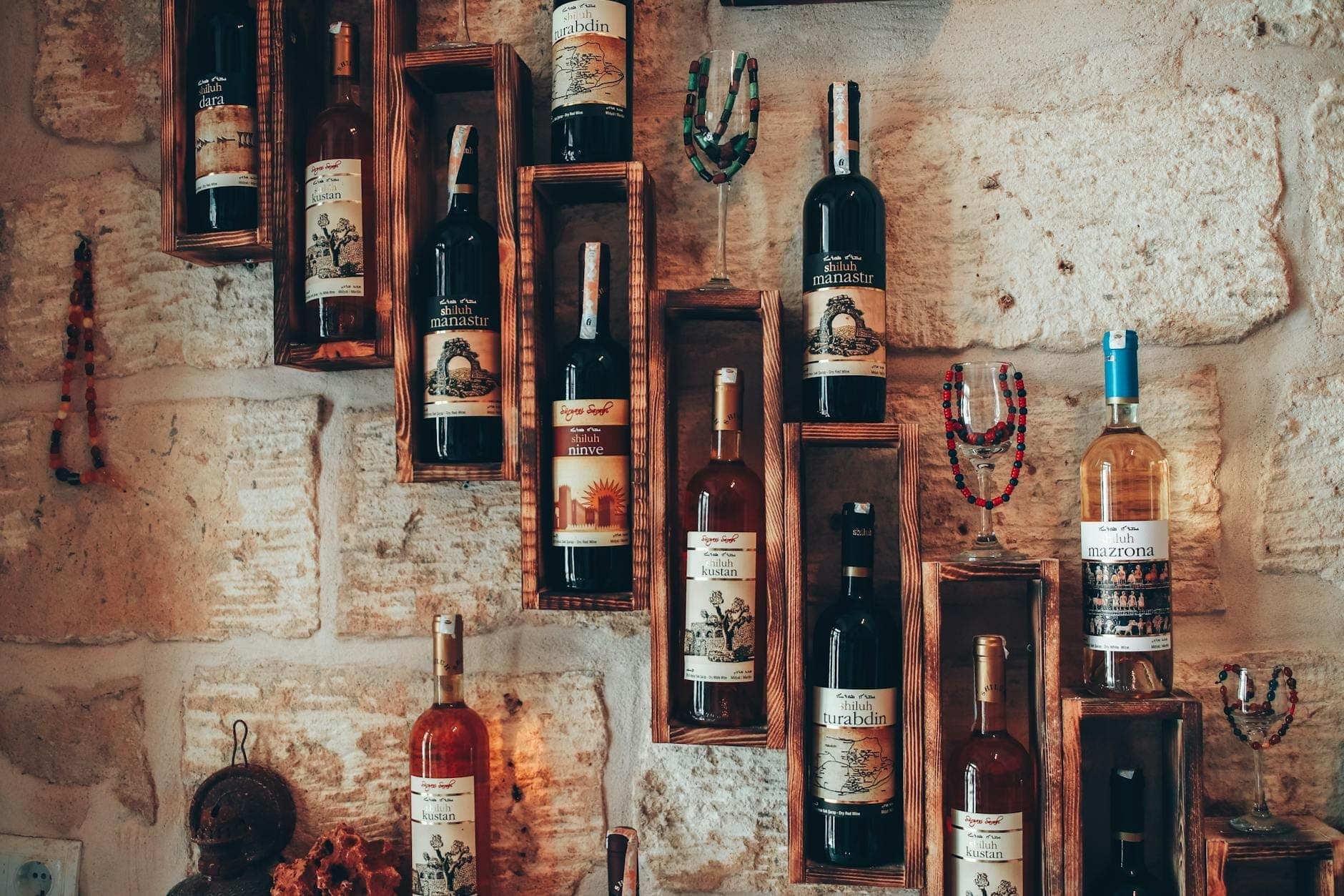 Weinflaschen auf rustikalen Holzregalen vor einer Steinwand in warmem Licht – die Atmosphäre eines Weinmuseums oder Weinkellers.