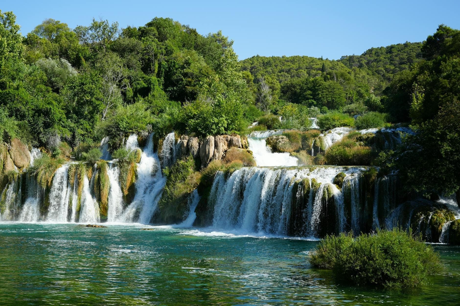 Vue panoramique des principales cascades du parc national de Krka se déversant sur les rochers dans une eau turquoise, entourées d'une forêt verdoyante par une journée ensoleillée.
