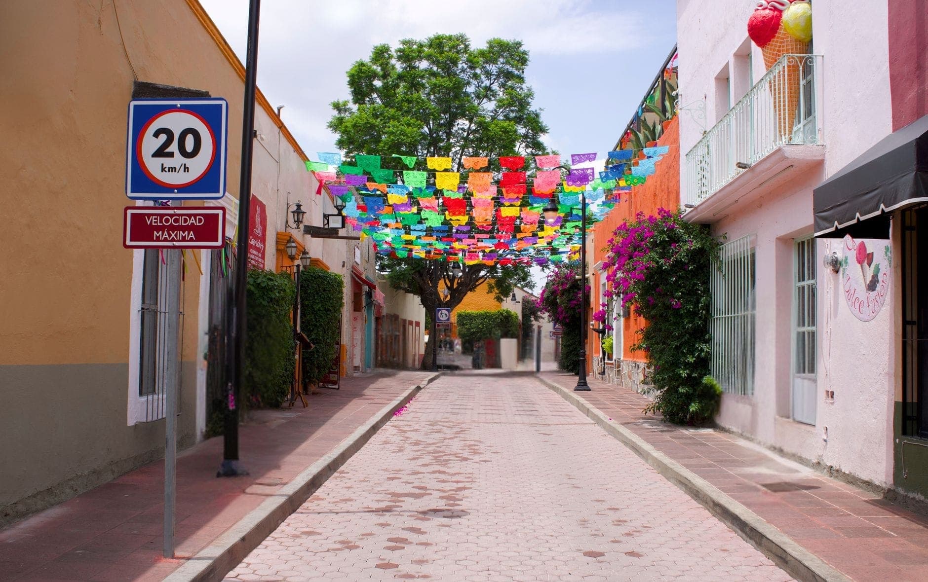 ถนนหินกรวดที่เรียงรายด้วยอาคารสีสันสดใสและธง papel picado แสนสวยงามเหนือศีรษะในเมืองเล็กๆ ของเม็กซิโก
