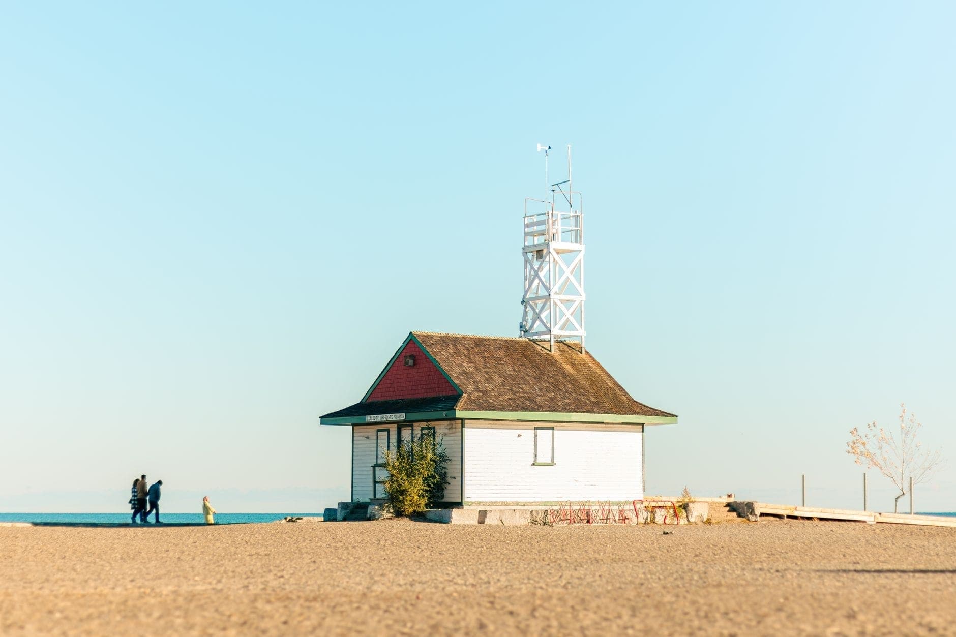 Una spiaggia sabbiosa con l'iconica Leuty Lifeguard Station e alcune persone che camminano vicino al lago Ontario in una giornata serena.