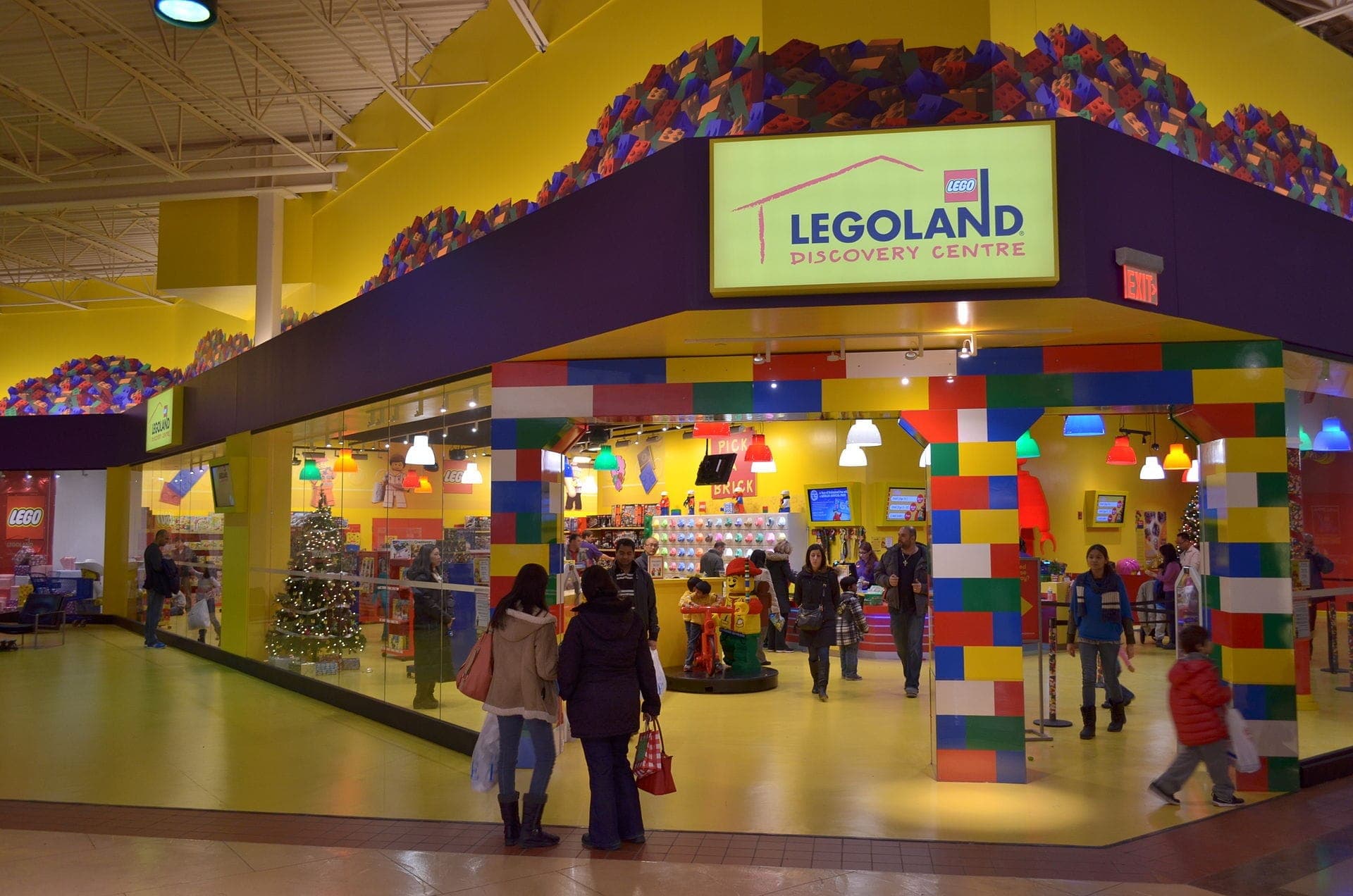 Entrada al LEGOLAND Discovery Centre Toronto en Vaughan Mills, con un arco de ladrillos LEGO de colores, paredes amarillas brillantes y familias entrando a la atracción.