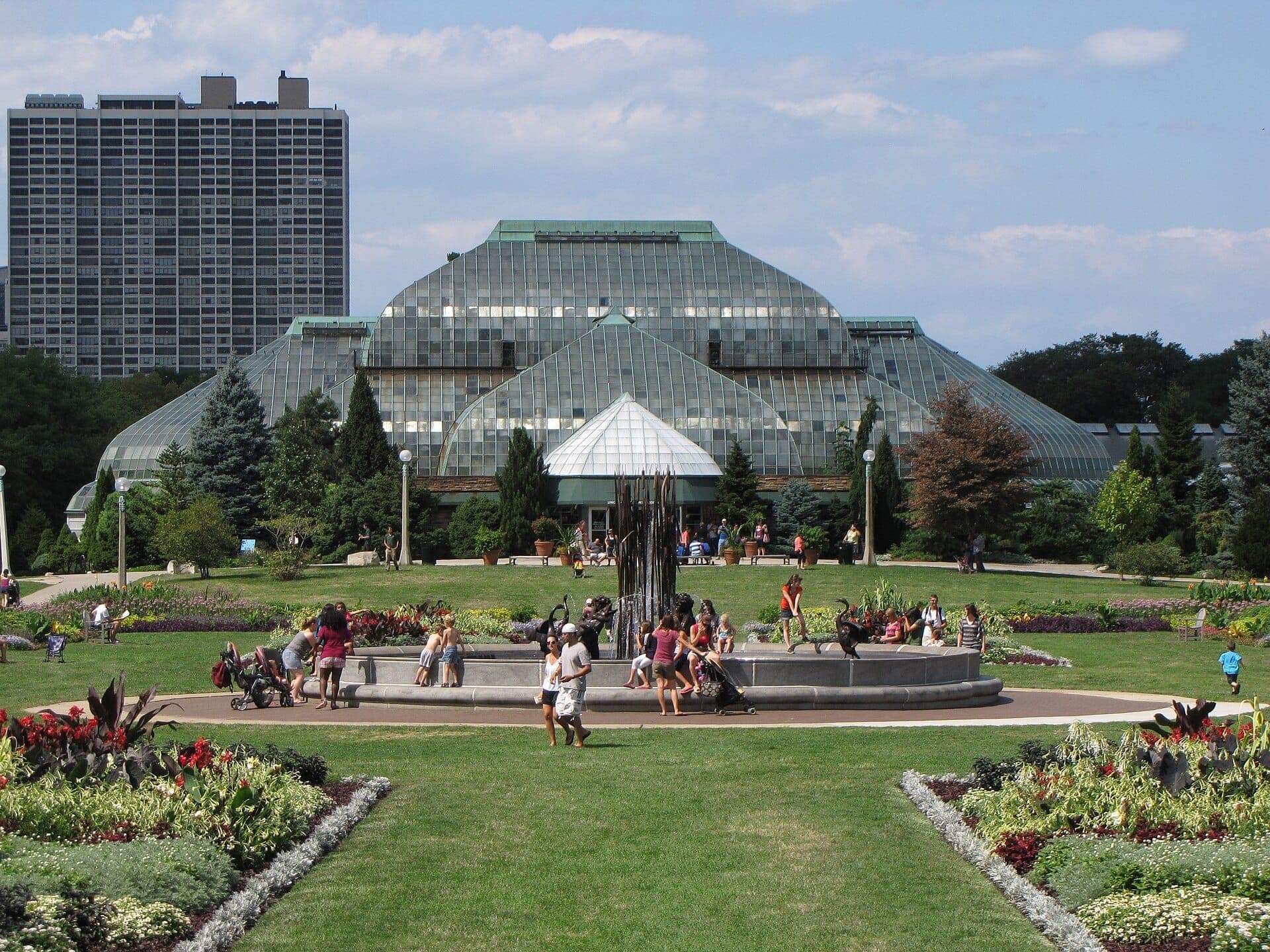 The Lincoln Park Conservatory’s distinctive Victorian glass structure surrounded by landscaped gardens and busy visitors on a sunny Chicago afternoon.