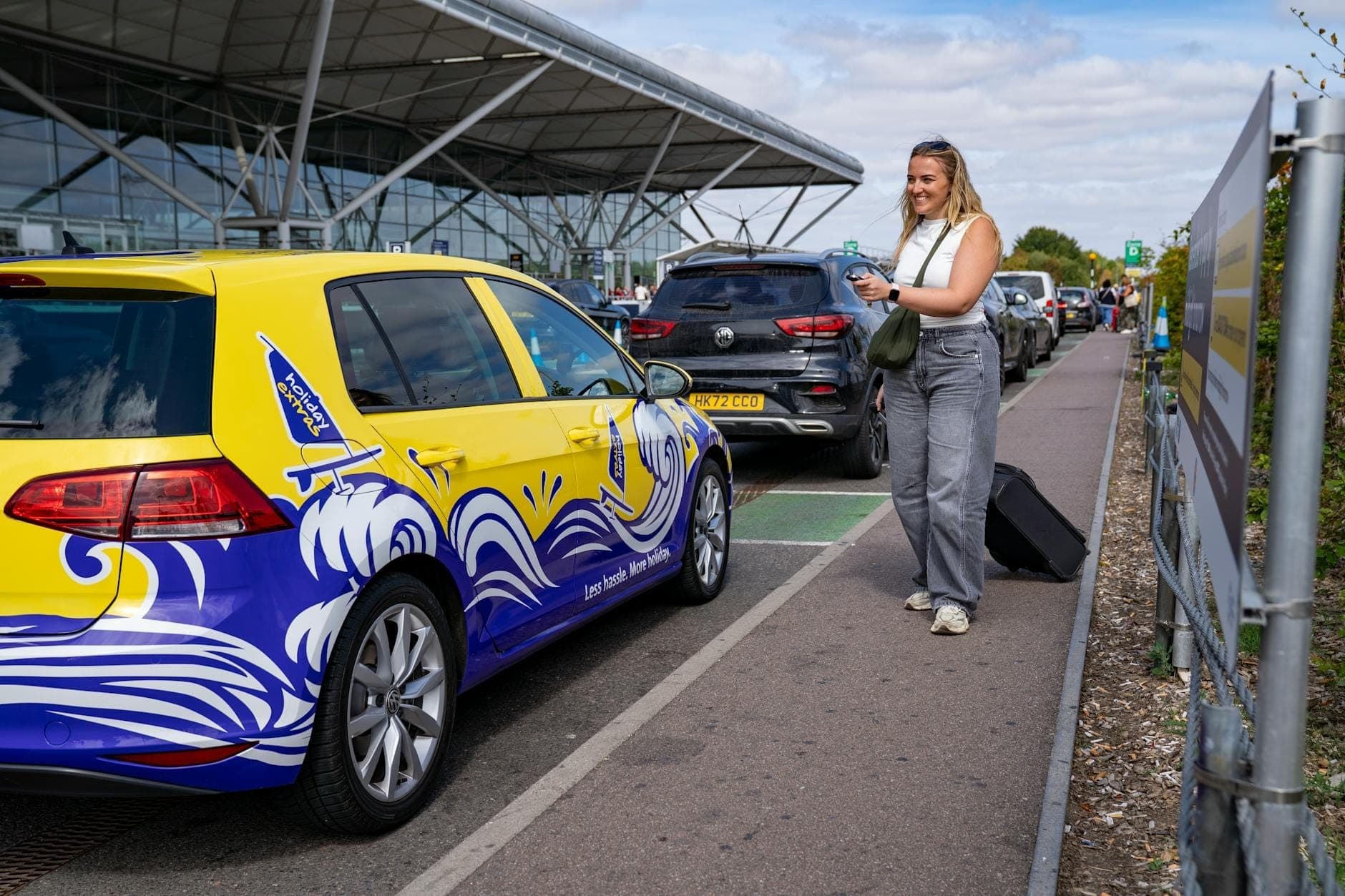 Una persona con una valigia si trova fuori da un moderno terminal aeroportuale accanto a un taxi colorato, suggerendo il trasporto terrestre in aeroporto.