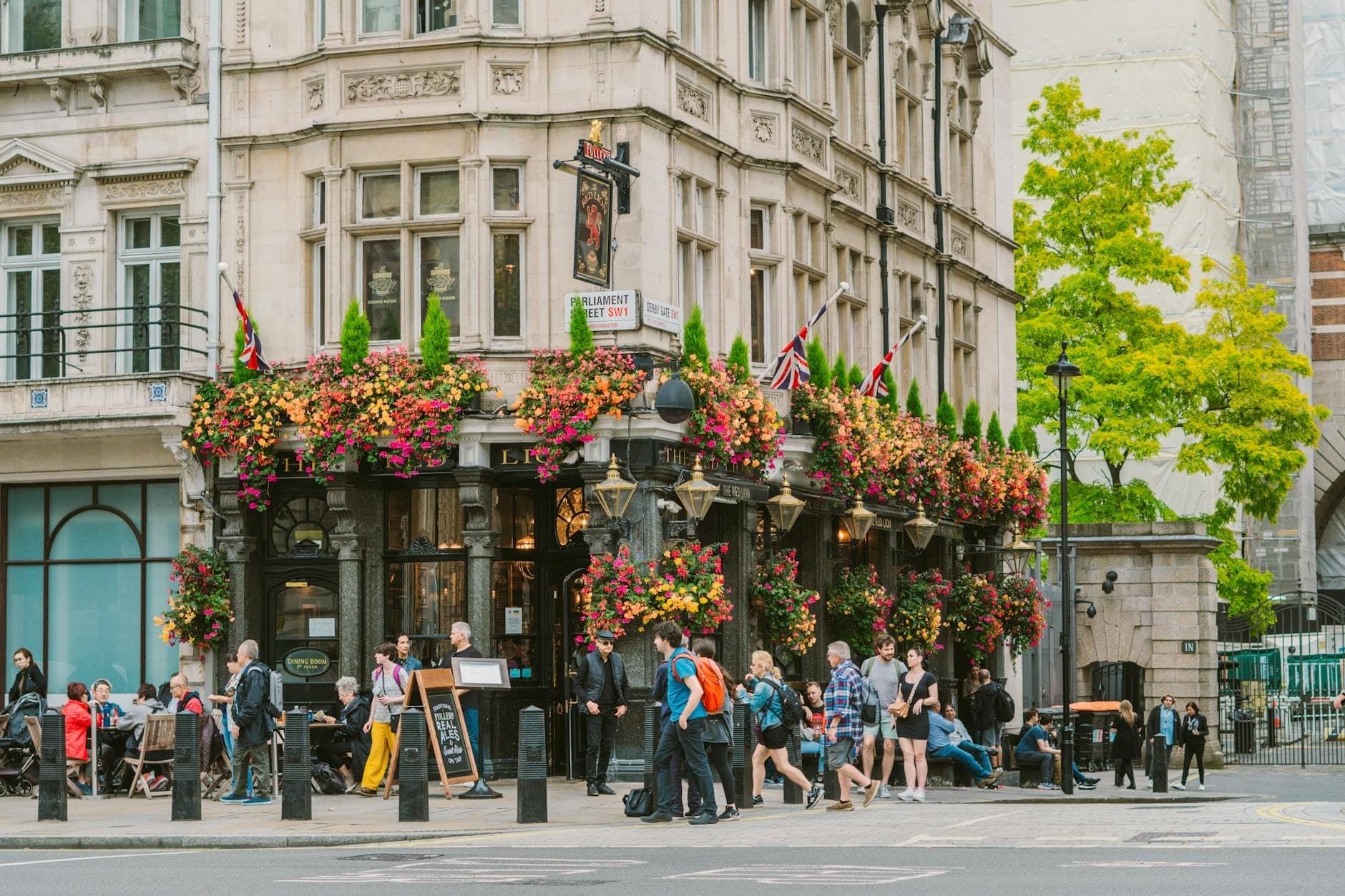 Klasyczny londyński pub z ozdobną architekturą, kolorowymi koszami kwiatów i ludźmi zebranymi na zewnątrz, cieszącymi się żywą atmosferą.