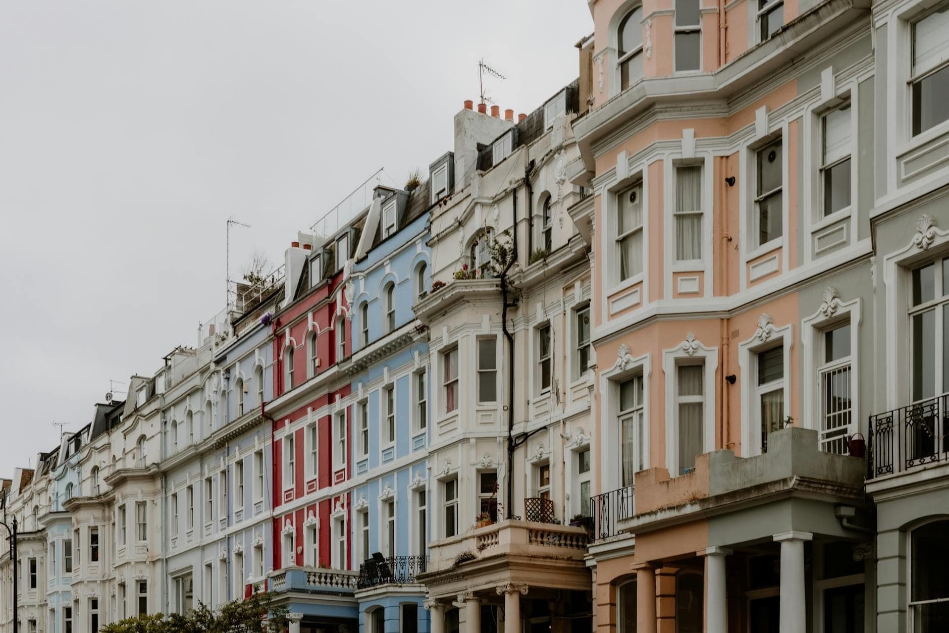 Hilera de casas adosadas clásicas de colores pastel en una calle de Londres bajo un cielo nublado, que muestra el carácter de los barrios de Londres.