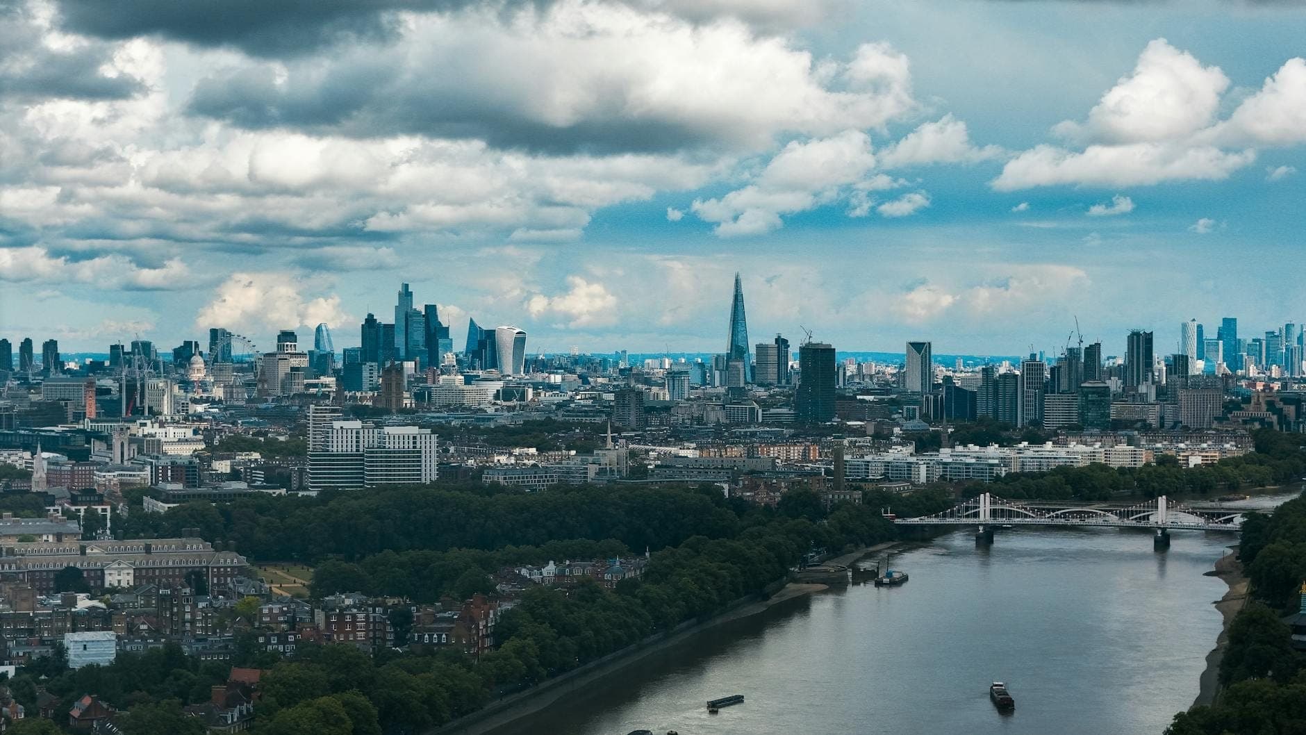 Vista aérea diurna y amplia del centro de Londres con el río Támesis, el horizonte urbano y destacados rascacielos bajo un cielo parcialmente nublado.