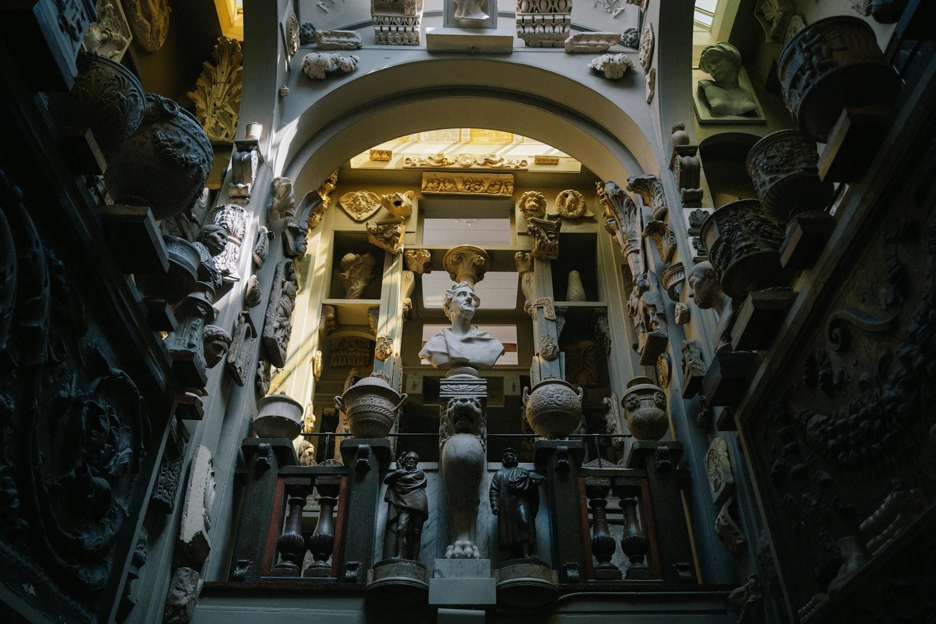 Eklektyczne wnętrze muzeum wypełnione klasycznymi popiersiam, rzeźbami i artefaktami pod dramatycznym łukiem i w naturalnym świetle.