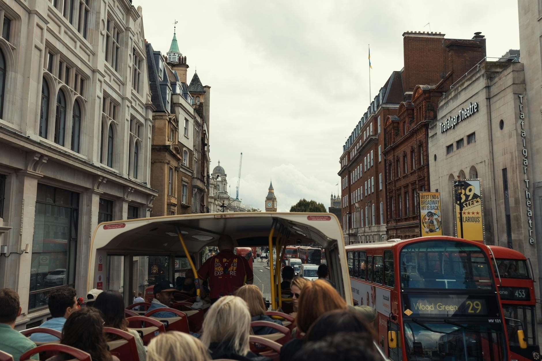 Überfülltes Oberdeck eines Londoner Hop-on-hop-off-Sightseeing-Busses, umgeben von belebten Stadtstraßen mit klassischer Londoner Architektur.