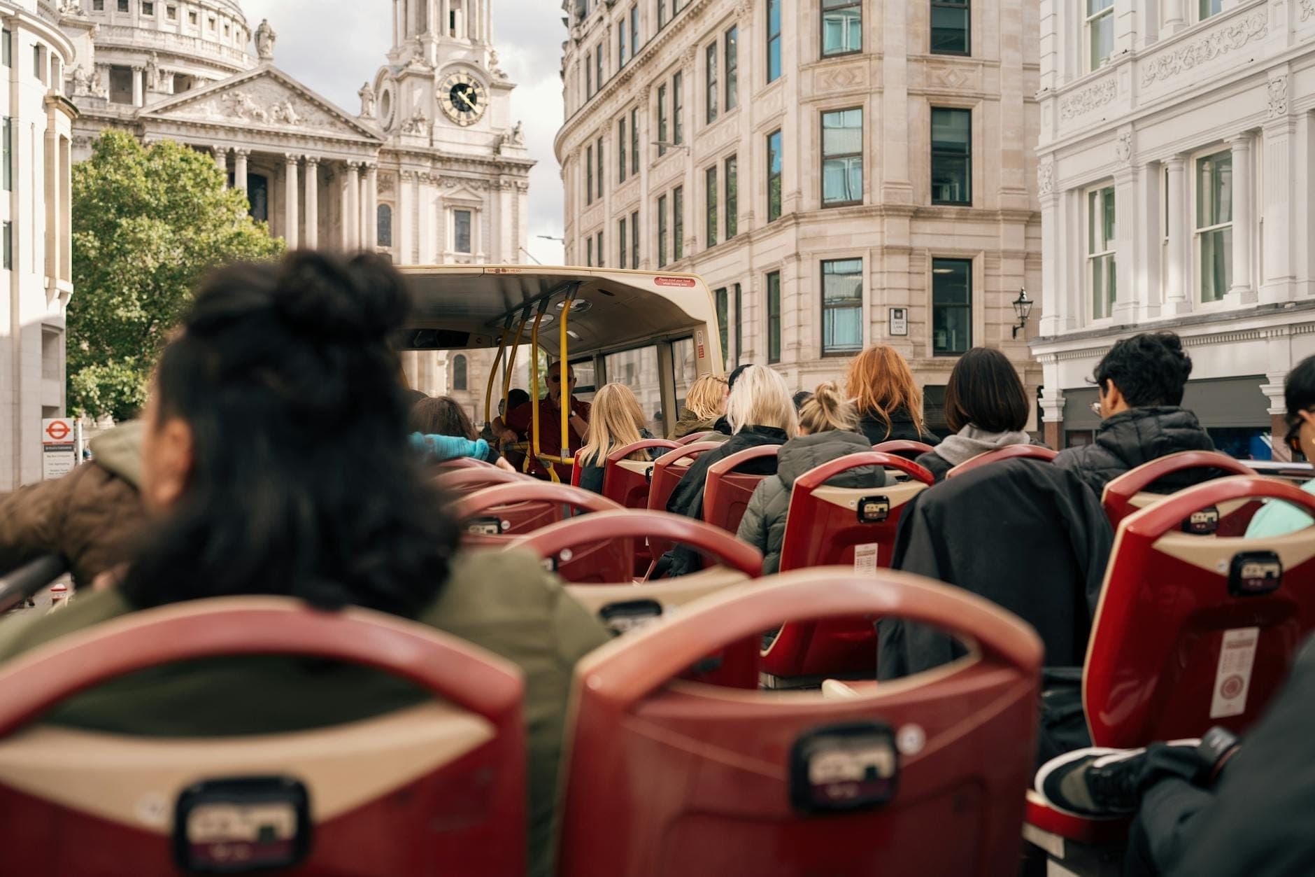Passagiere sitzen auf dem offenen Oberdeck eines roten Hop-on-Hop-off-Busses in London, der an historischen Steingebäuden und der St. Paul's Cathedral vorbeifährt.