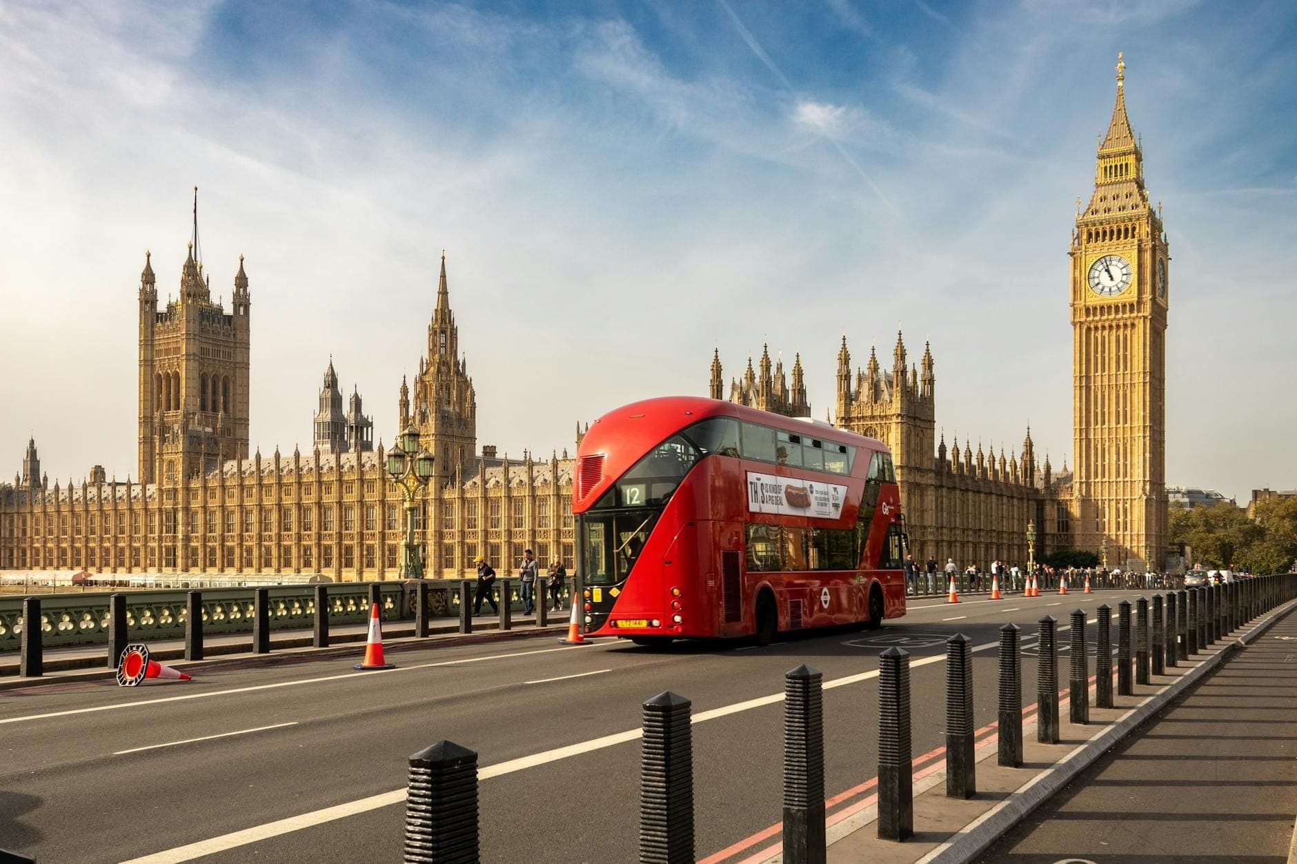 Ein roter Londoner Doppeldeckerbus fährt an Big Ben und den Houses of Parliament unter einem klaren Himmel vorbei und zeigt eine klassische Aussicht auf einer Sightseeing-Route.