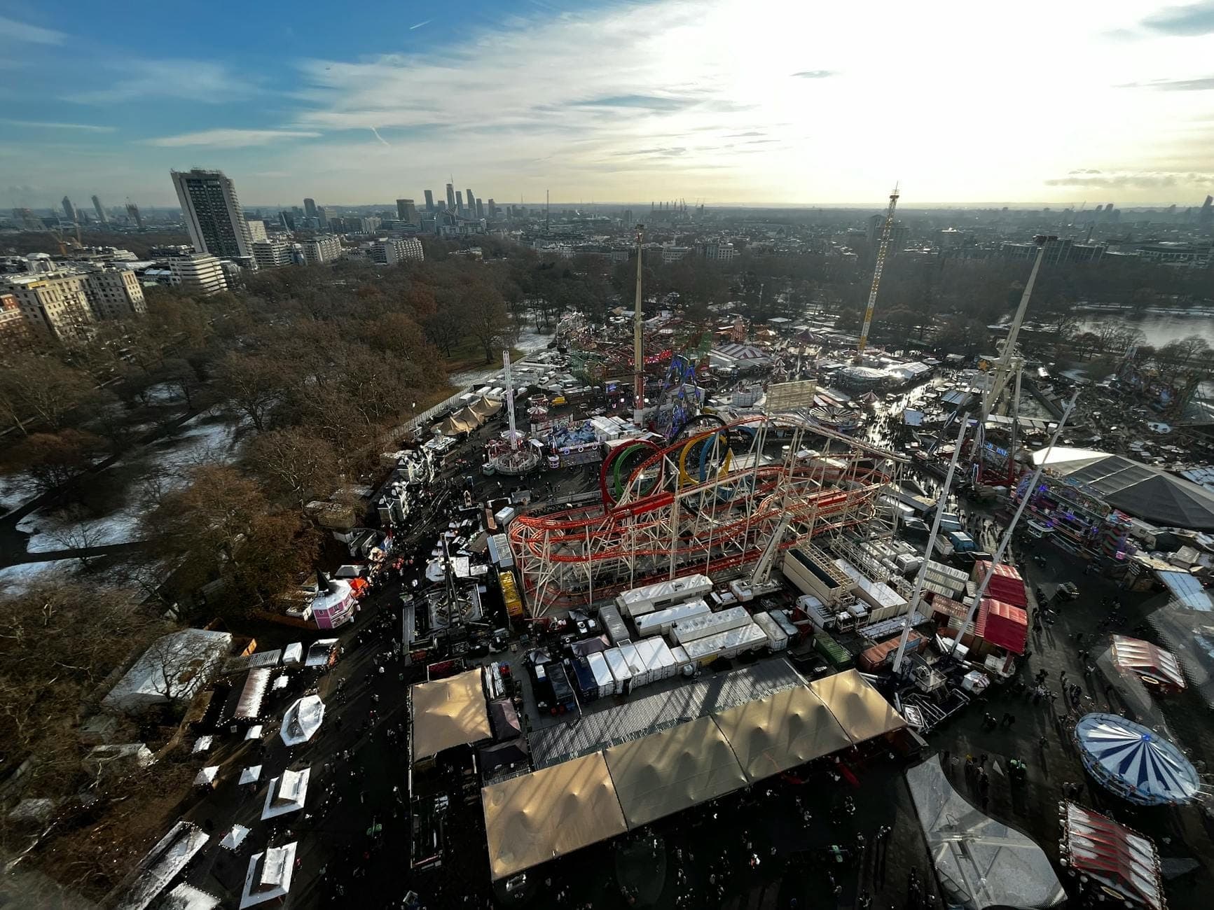 Widok z lotu ptaka na Hyde Park Winter Wonderland w Londynie z karuzelami, kolejkami górskimi, świątecznymi straganami i tłumami, z panoramą miasta w tle.