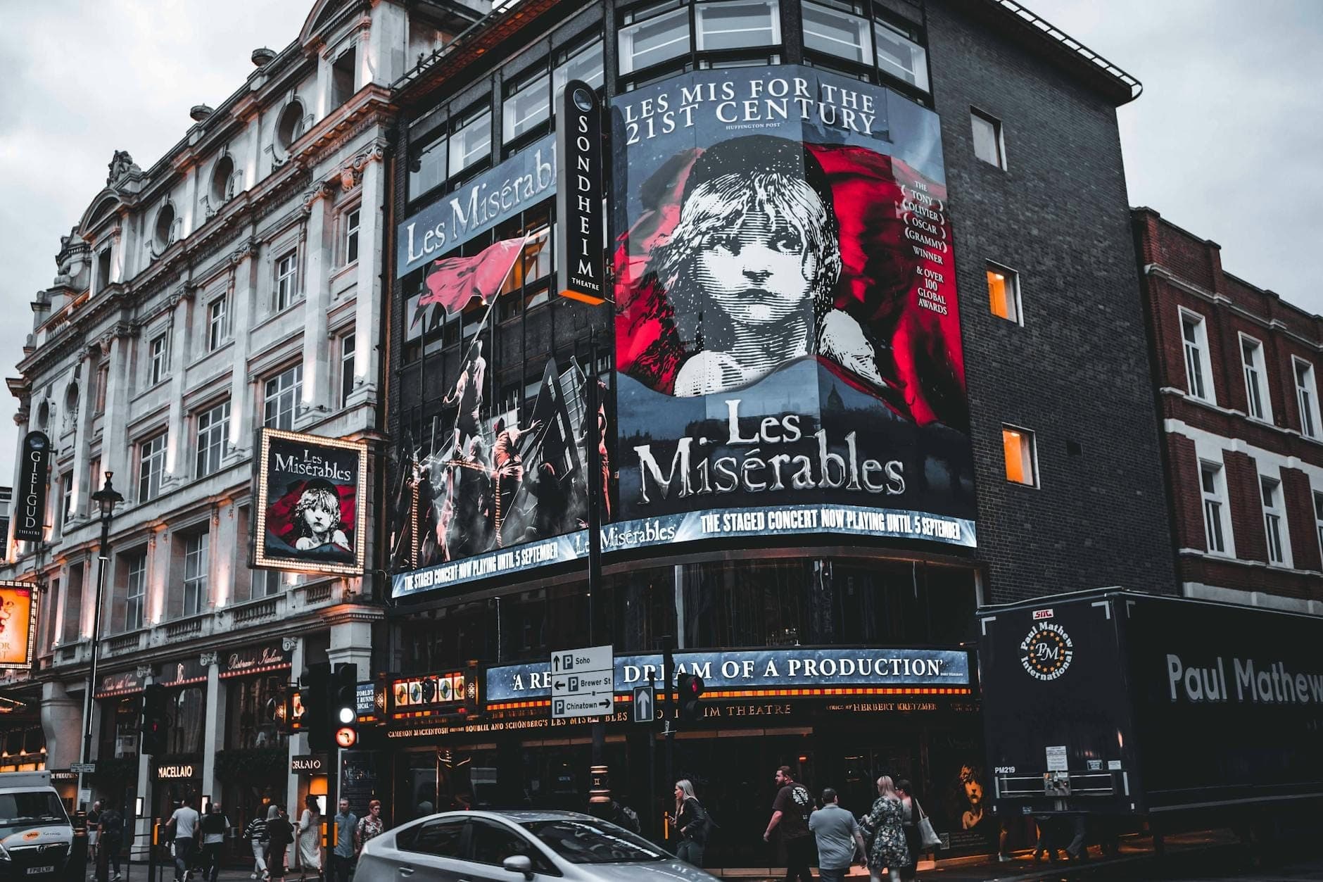 Fasada Sondheim Theatre w Londynie o zmierzchu, jasno oświetlona z dużymi szyldami Les Misérables i ludźmi spacerującymi na zewnątrz
