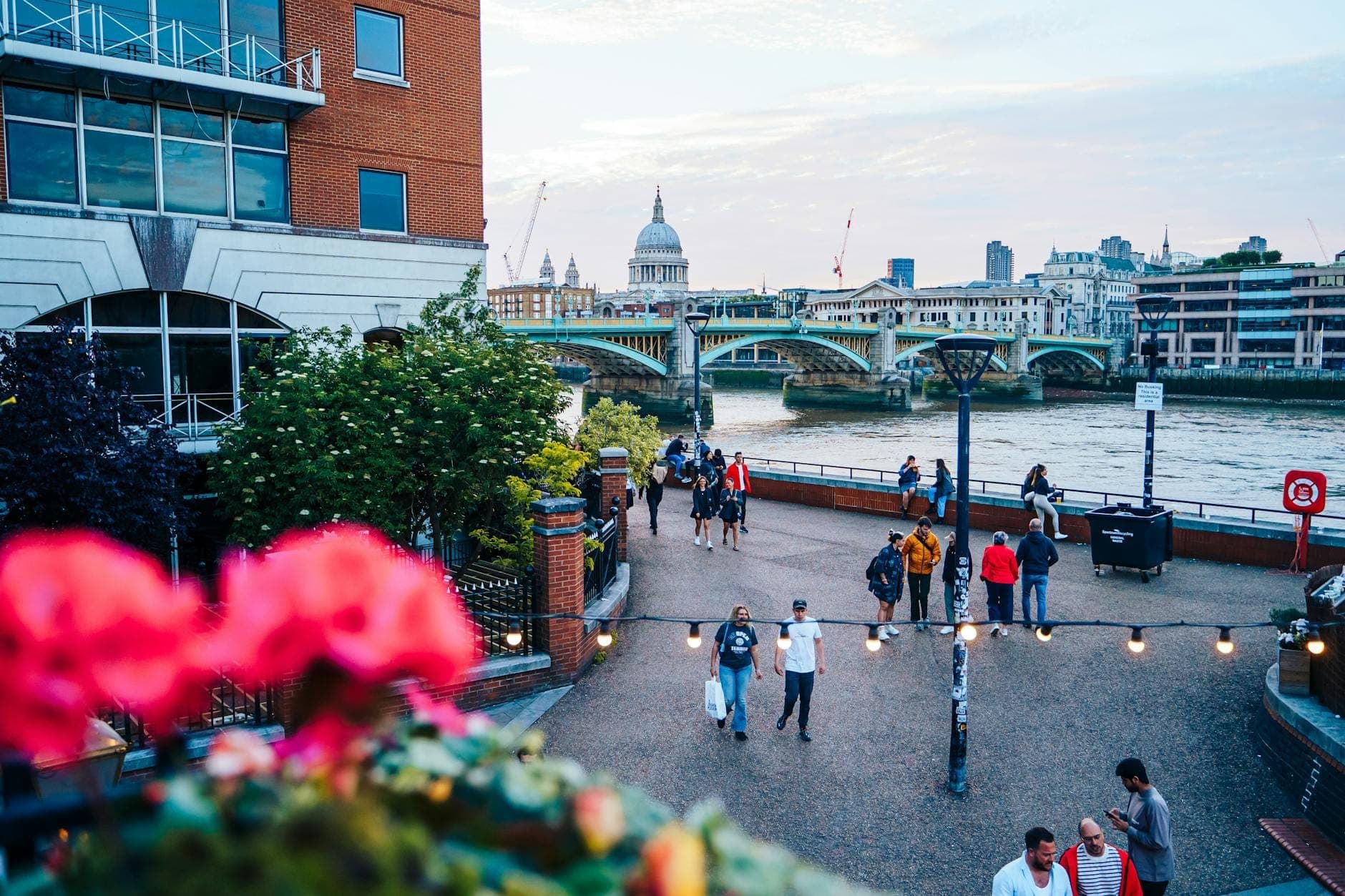 Personas paseando por el paseo fluvial junto al Támesis en Londres, con la Catedral de St. Paul's y un puente visibles al fondo.