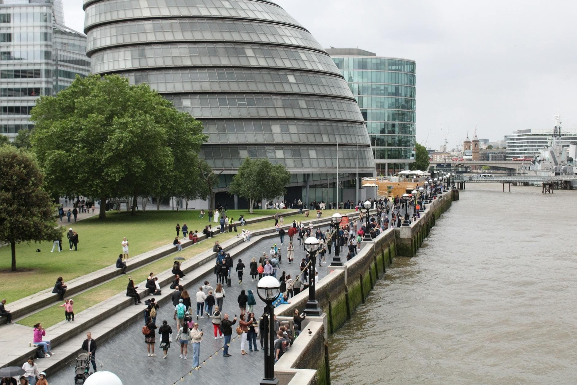 Personas caminando a lo largo del Támesis junto al London City Hall en un suave y nublado día de verano