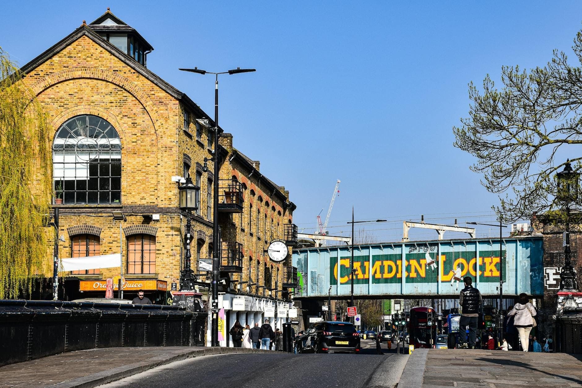 Vista di Camden Lock a Londra con l'iconico ponte ferroviario blu e giallo di Camden Lock, gli edifici del mercato e le persone che camminano nelle vicinanze.