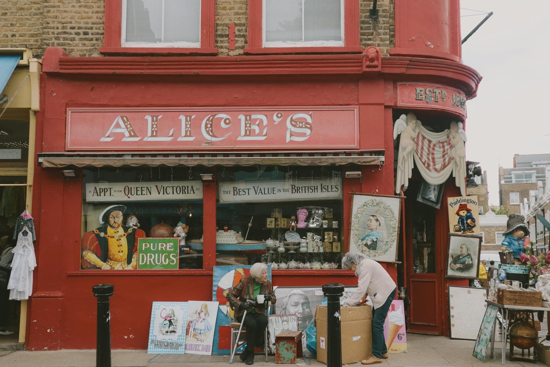 Rot gestrichene Ladenfront von Alice's Antiquitätengeschäft in London mit Vintage-Artikeln und stöbernden Menschen draußen.