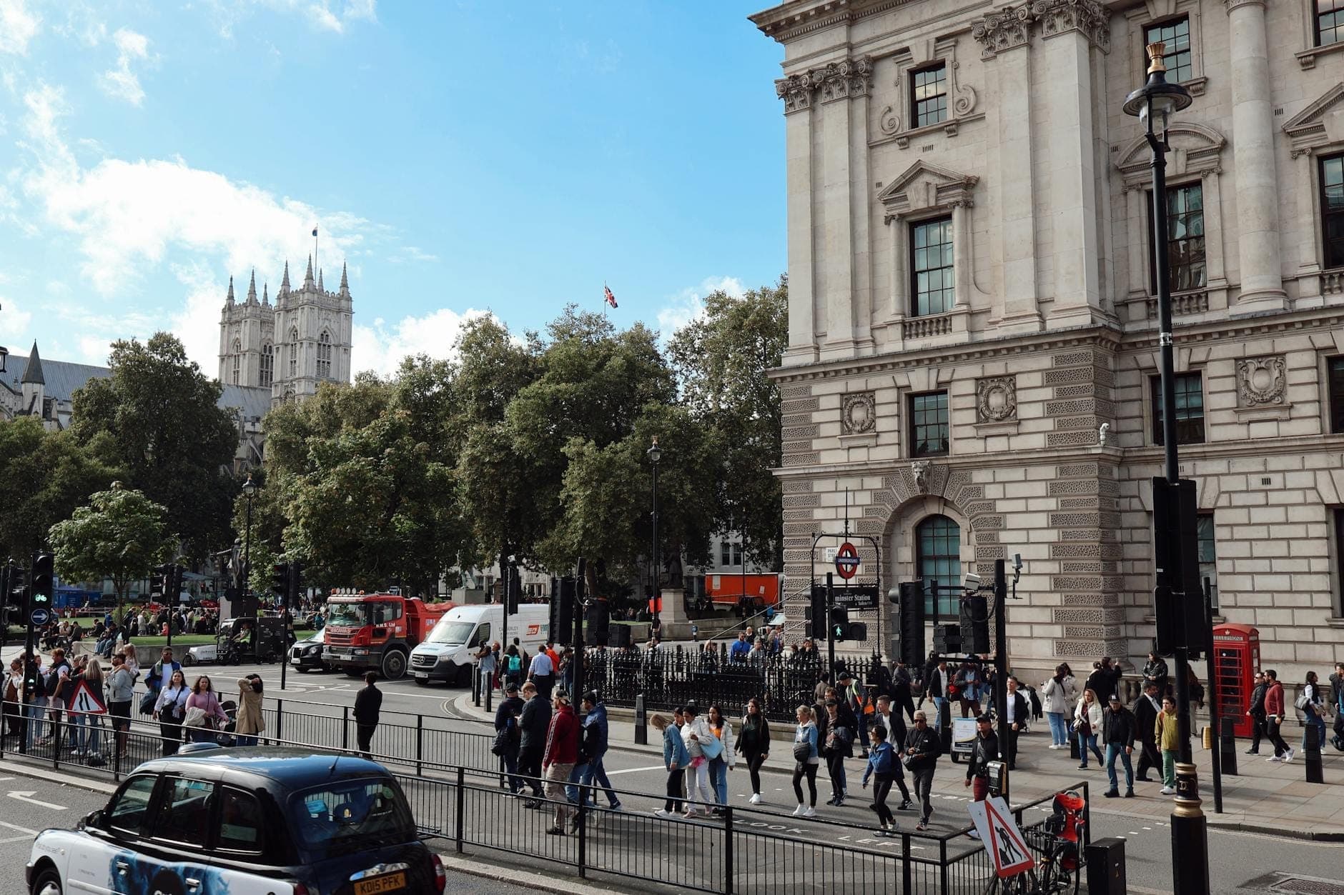 Ruchliwa scena uliczna w Londynie z Westminster Abbey w tle, przechodniami, ruchem ulicznym i klasycznymi miejskimi budynkami.