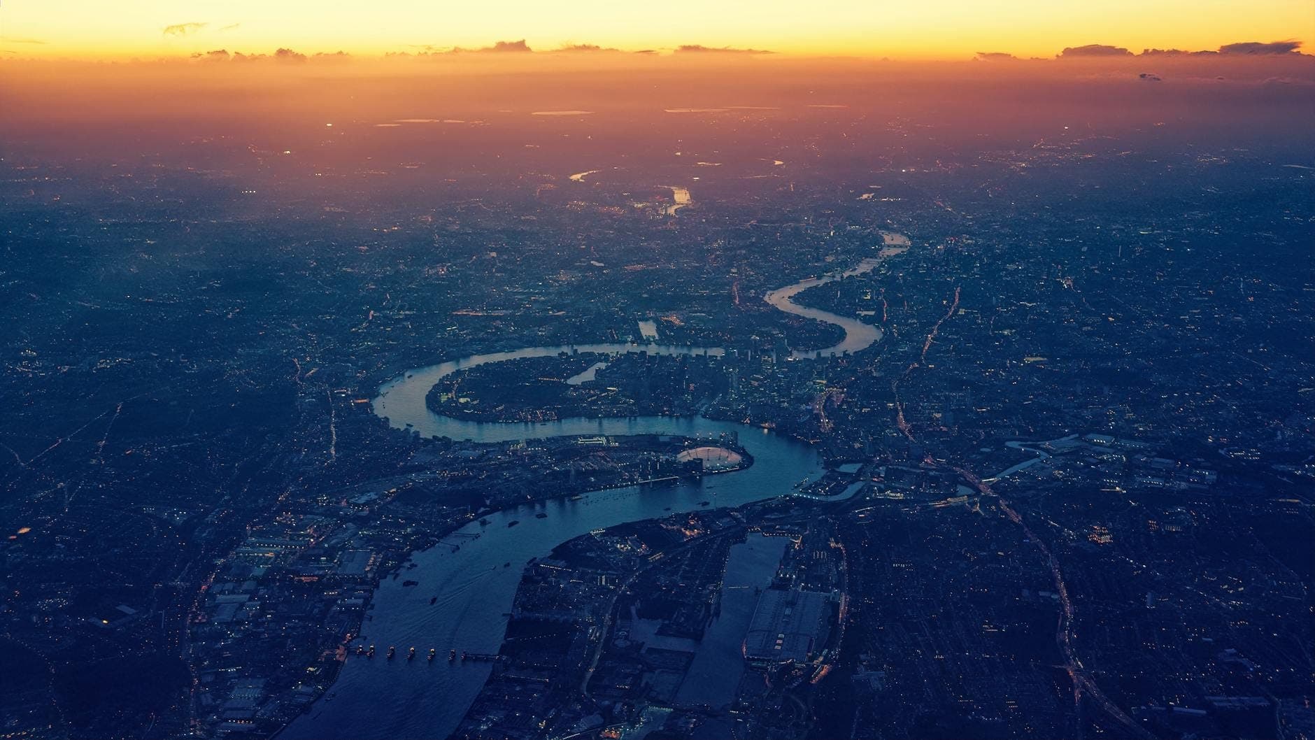 Aerial view of the River Thames winding through the city of London at sunset, showing the river’s distinct curves and urban landscape.