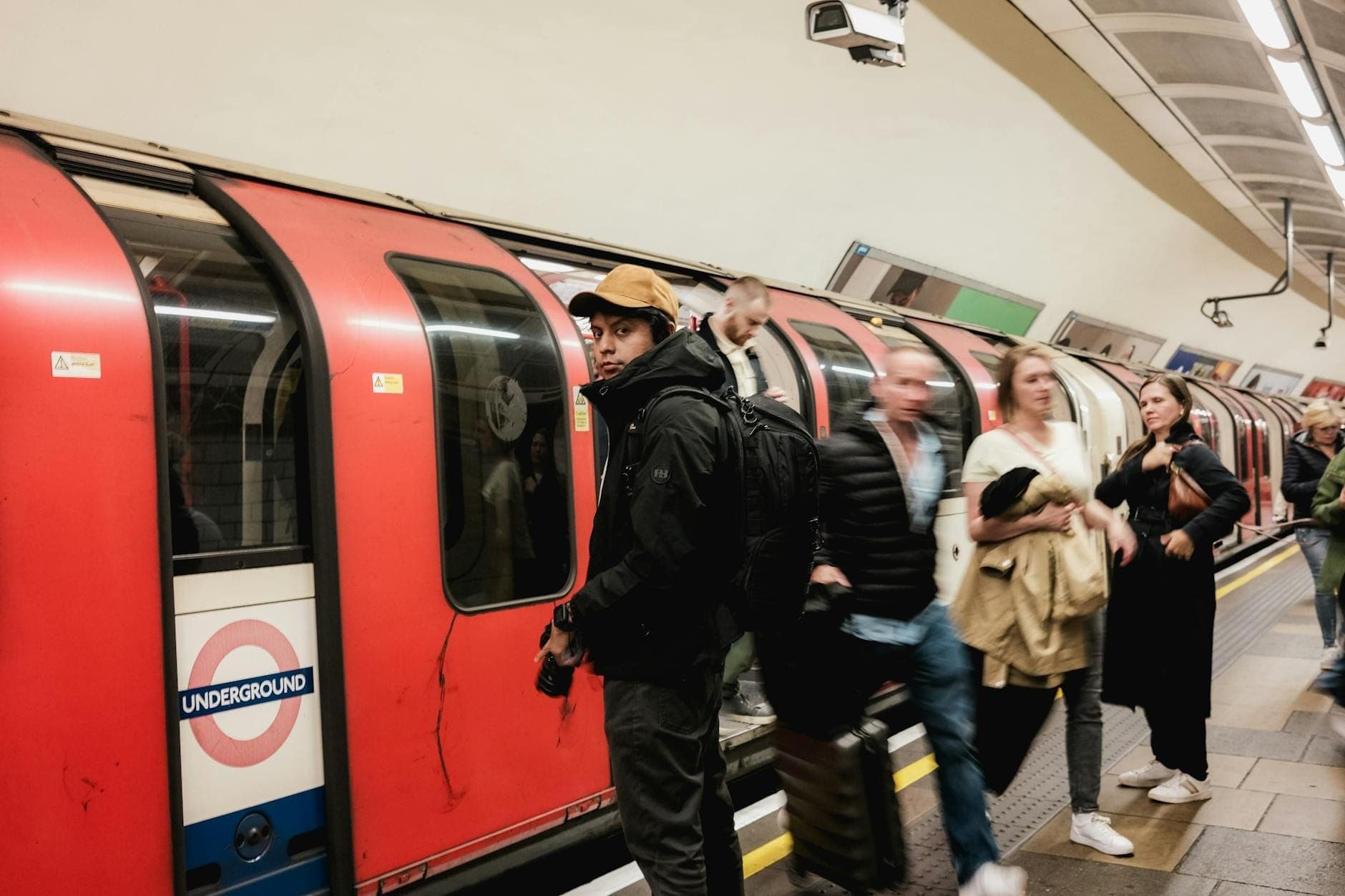 Quai bondé dans une station du London Underground avec des passagers montant à bord d'un train rouge du Tube, le roundel de l'Underground clairement visible.
