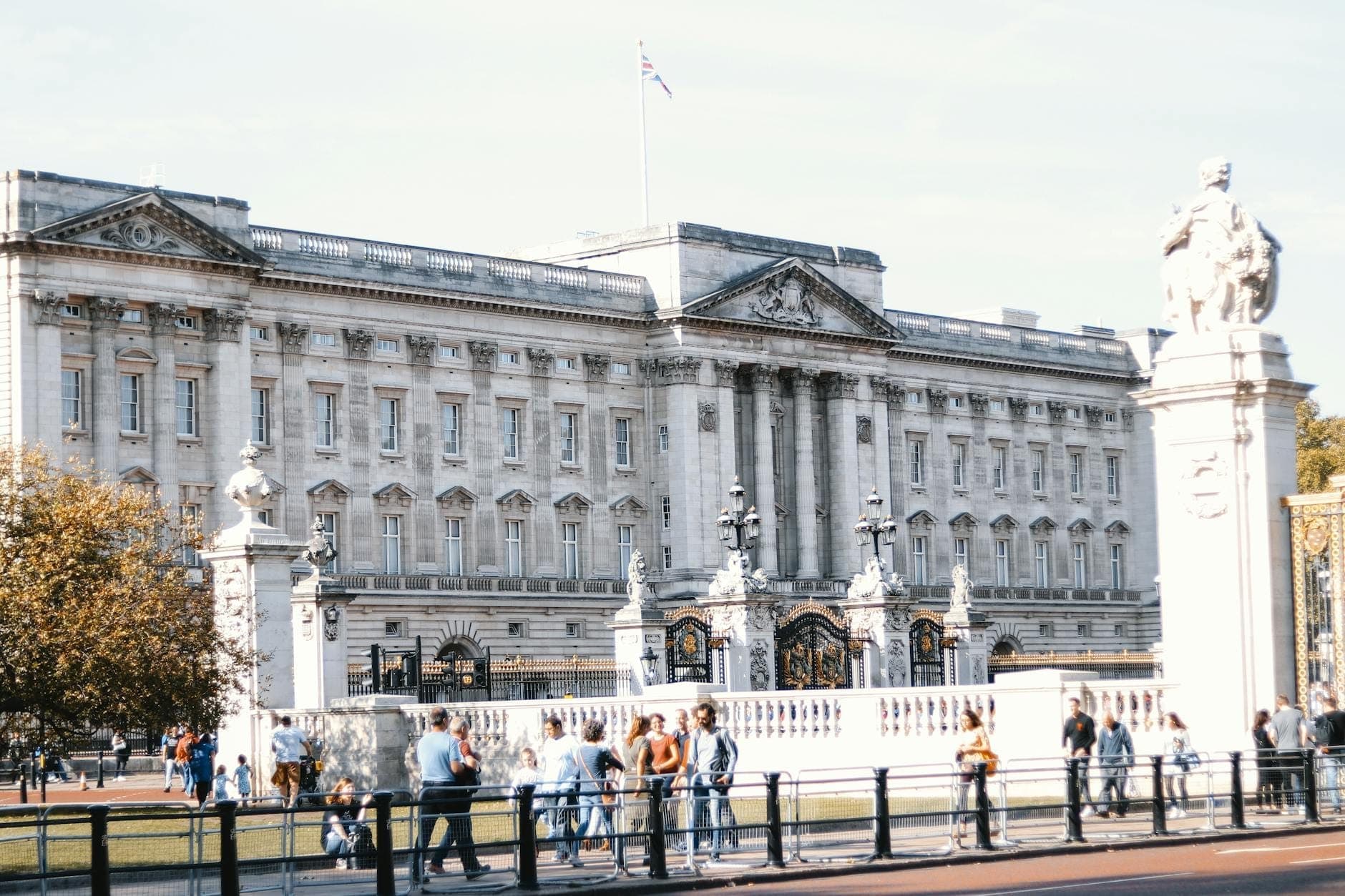 Des touristes se promenant devant Buckingham Palace par une journée ensoleillée, avec un ciel dégagé et des foules visibles.