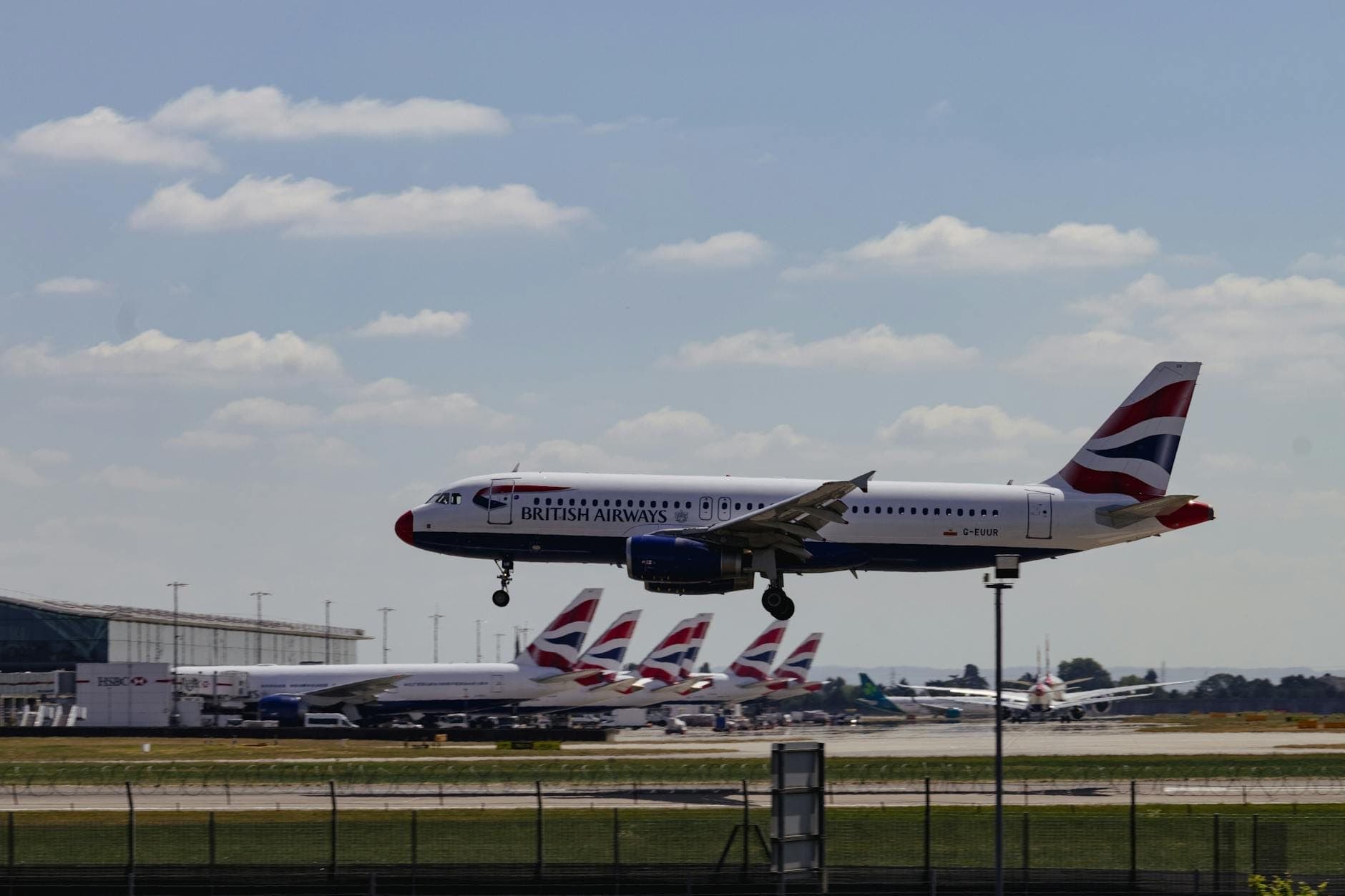 Samolot British Airways lądujący na lotnisku z kilkoma innymi samolotami British Airways widocznymi przy bramkach terminalu.