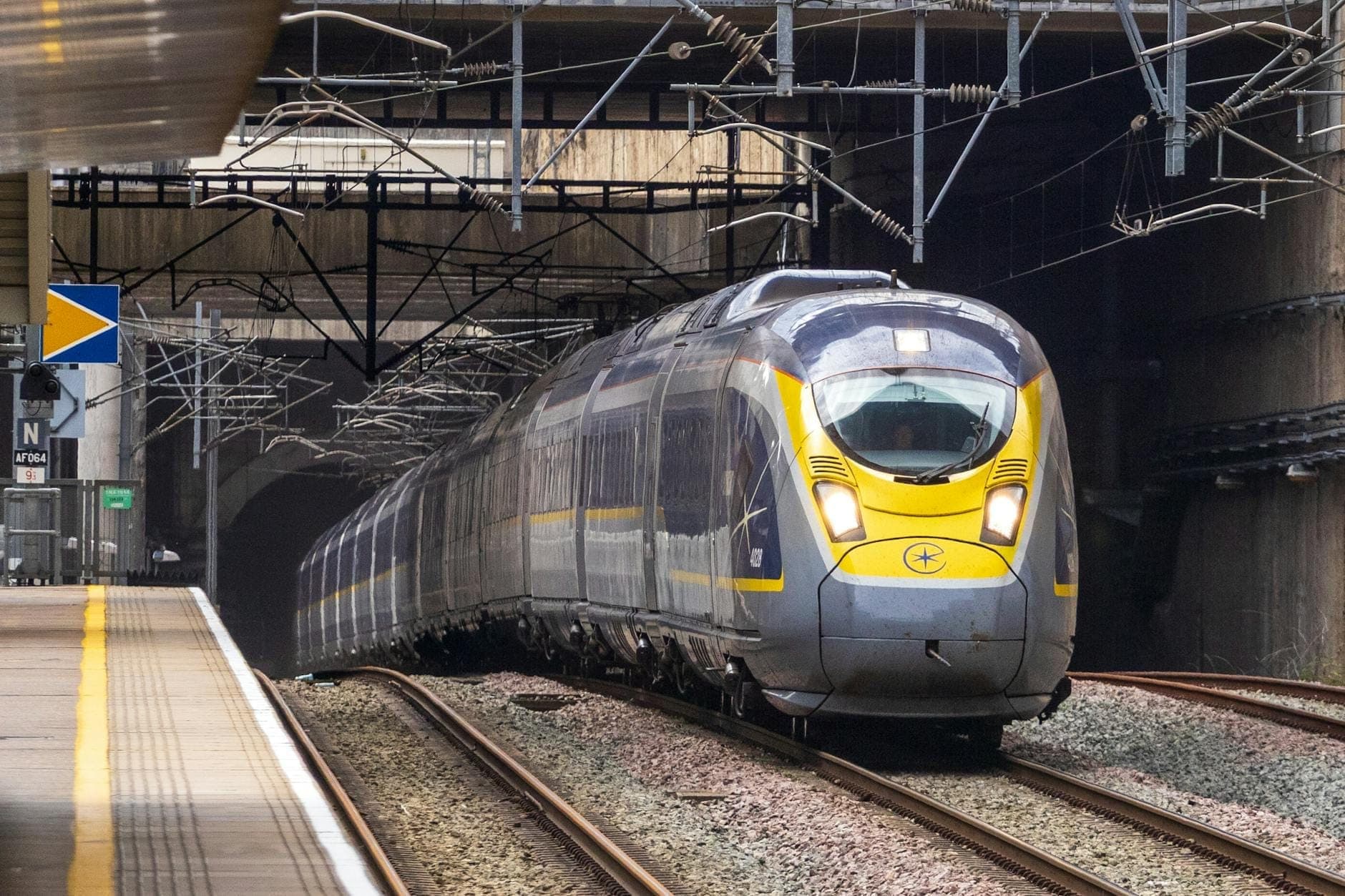 Pociąg Eurostar wjeżdża na stację — widok z przodu, tory i tunel, symbol szybkich podróży między miastami.