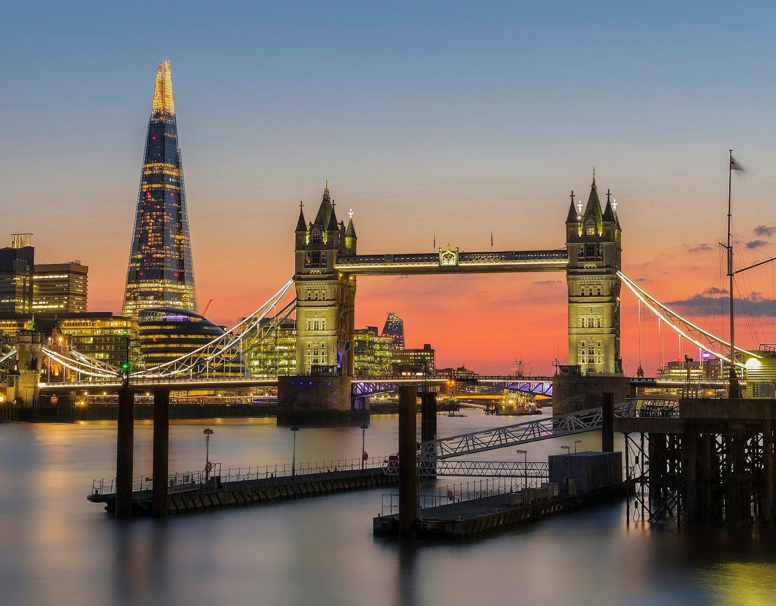 View of Tower Bridge and the Shard at sunset with lights reflected on the River Thames, an iconic and recognizable London cityscape.