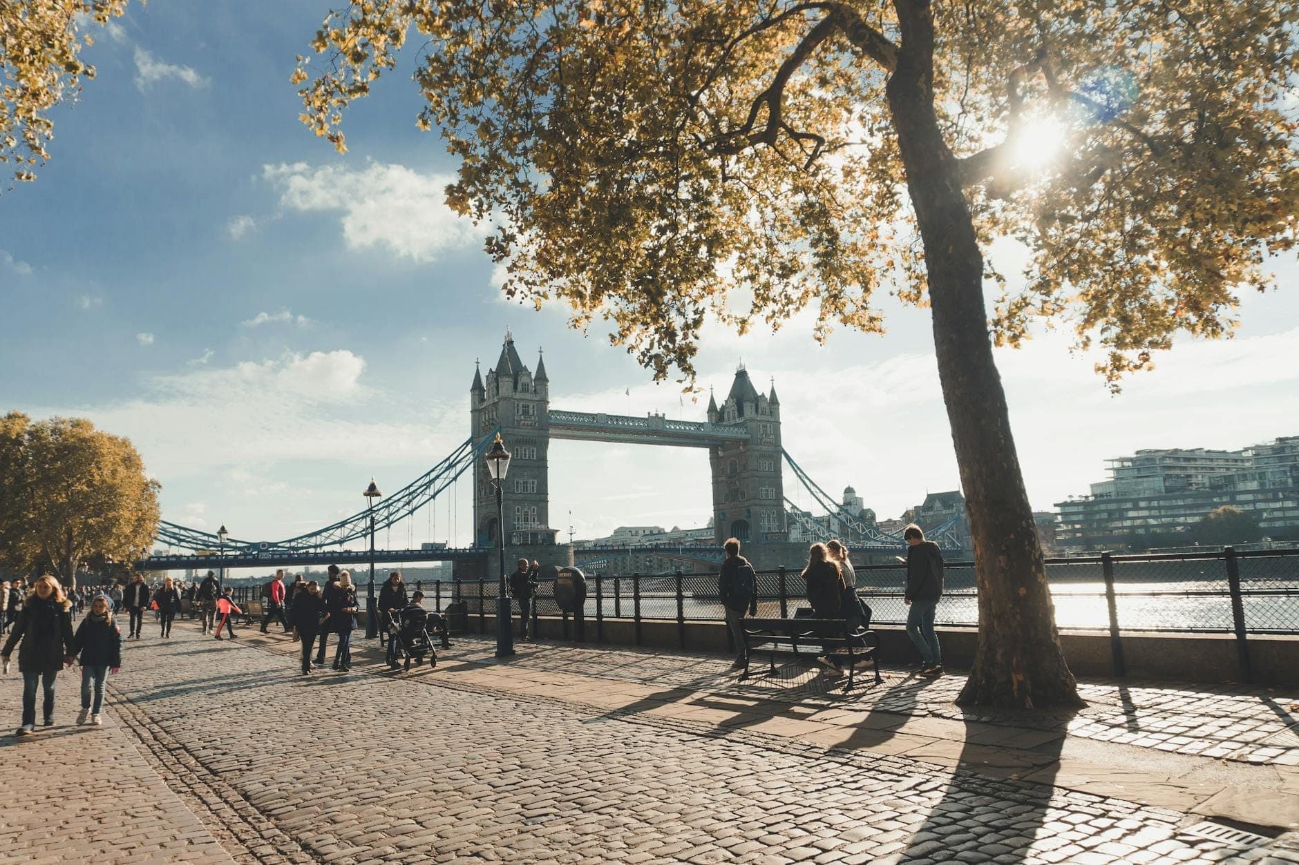 Menschen spazieren entlang des Thames Path, im Hintergrund die Tower Bridge an einem sonnigen Tag in London.