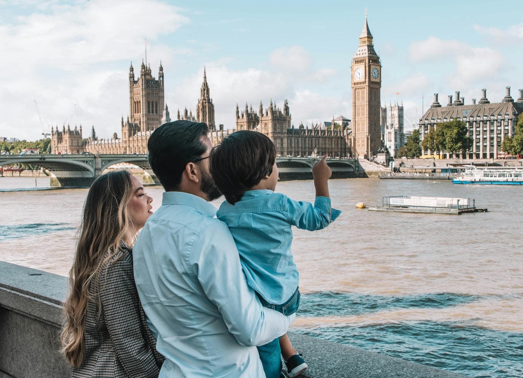 Famiglia con bambino piccolo che guarda il Tamigi verso il Big Ben e il Parlamento in una giornata luminosa a Londra.