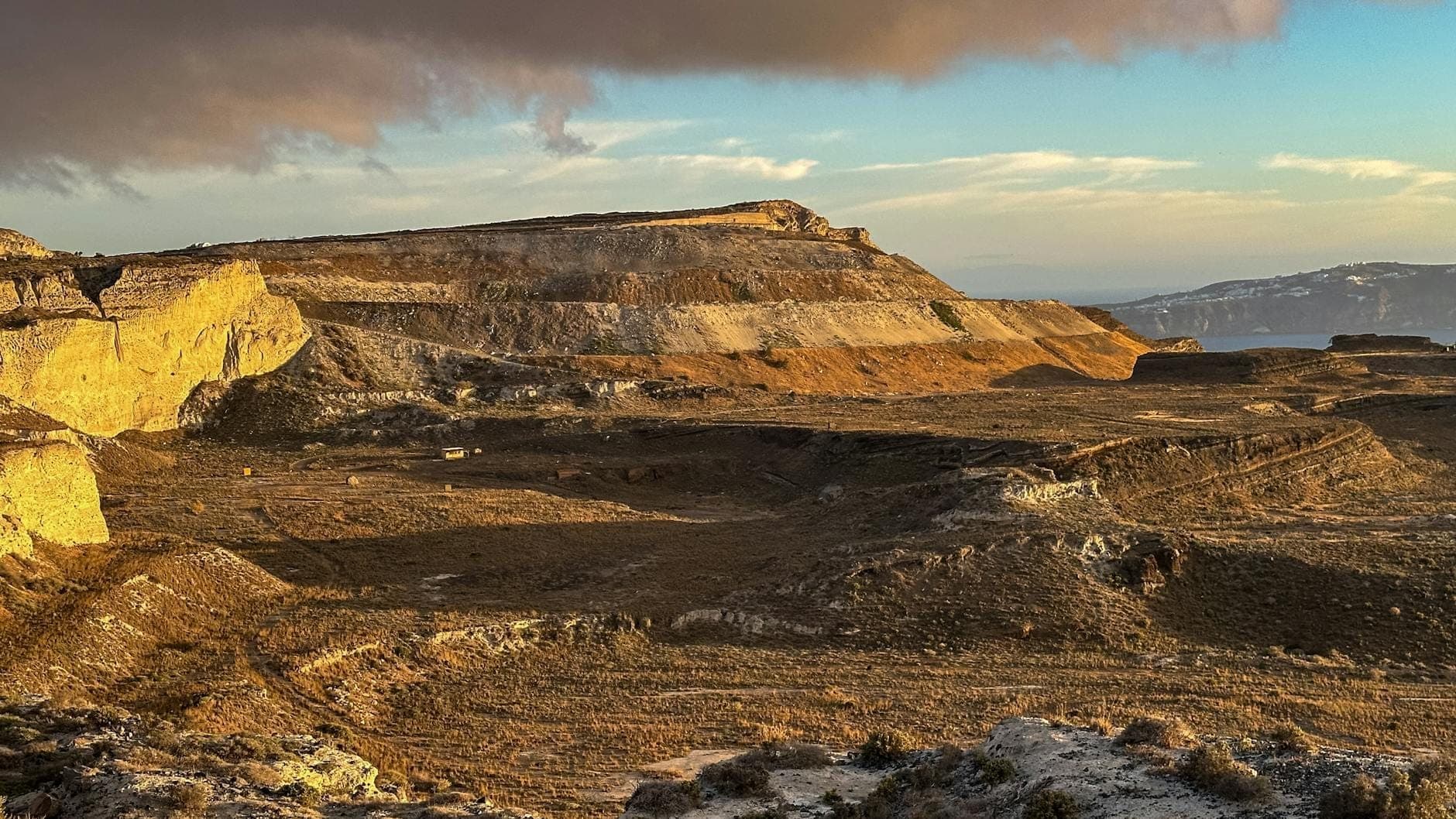 Sonnenbeschienene Vulkanlandschaft Santorinis mit dramatisch geschichteten Klippen und weitem Blick – eine Kulisse, die an die rätselhafte Vergangenheit der Insel und die Atlantis-Legenden erinnert.