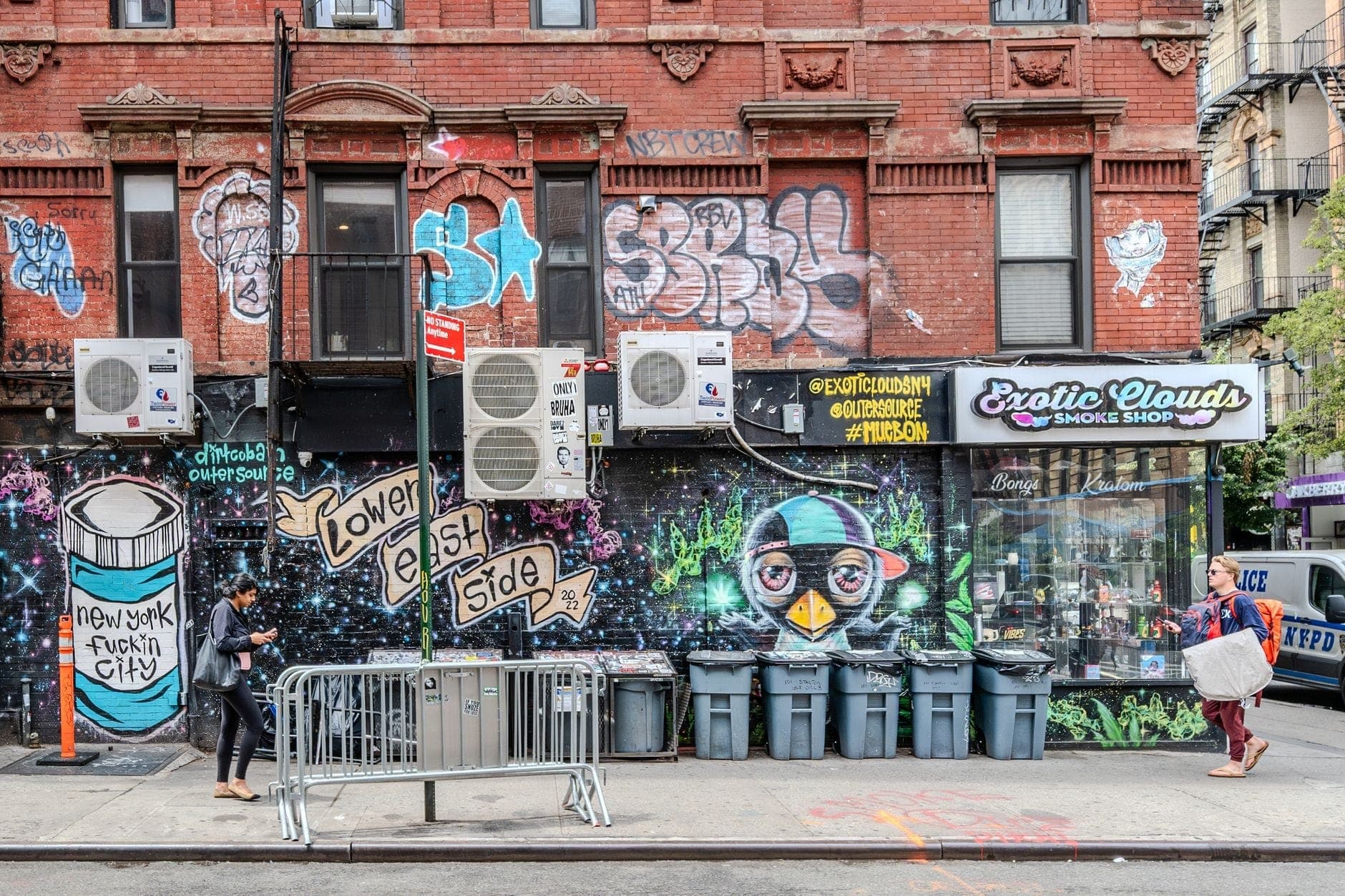 งานศิลปะข้างถนนและกราฟฟิตีสีสันสดใสปกคลุมอาคารอิฐในย่าน Lower East Side ของ Manhattan พร้อมร้านค้าและคนเดินถนนที่สัญจรไปบนทางเท้า