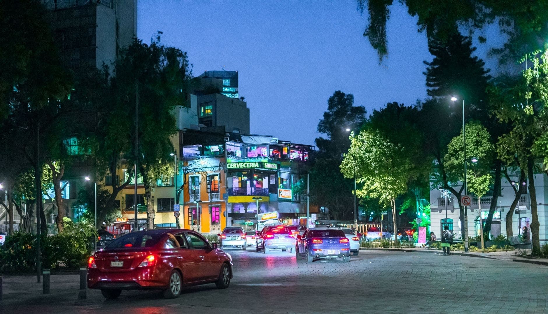 วิวถนนในย่านที่คึกคักของ Mexico City ยามค่ำคืน พร้อมรถยนต์และอาคารที่สว่างไสว สะท้อนชีวิตเมืองยามราตรี