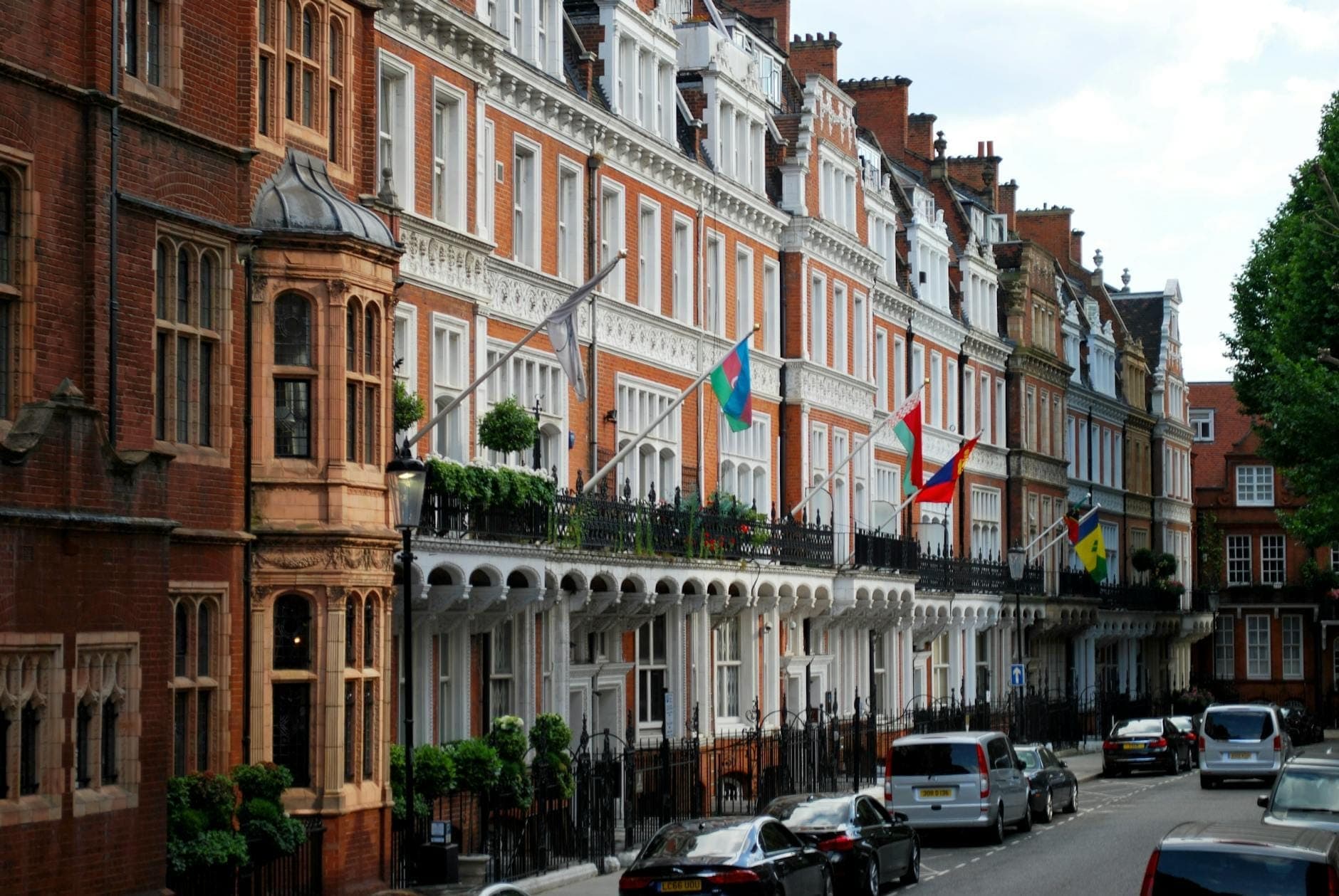 Londra'nın üst sınıf bir semtinde sakin bir sokakta bayraklar, süslü balkonlar ve lüks arabalar bulunan zarif sıra evler.