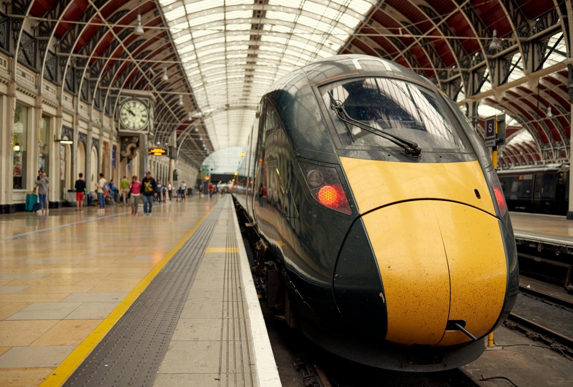 London Paddington İstasyonu'nun kemerli çatılı peronunda modern yüksek hızlı tren ve yakınındaki yolcular.