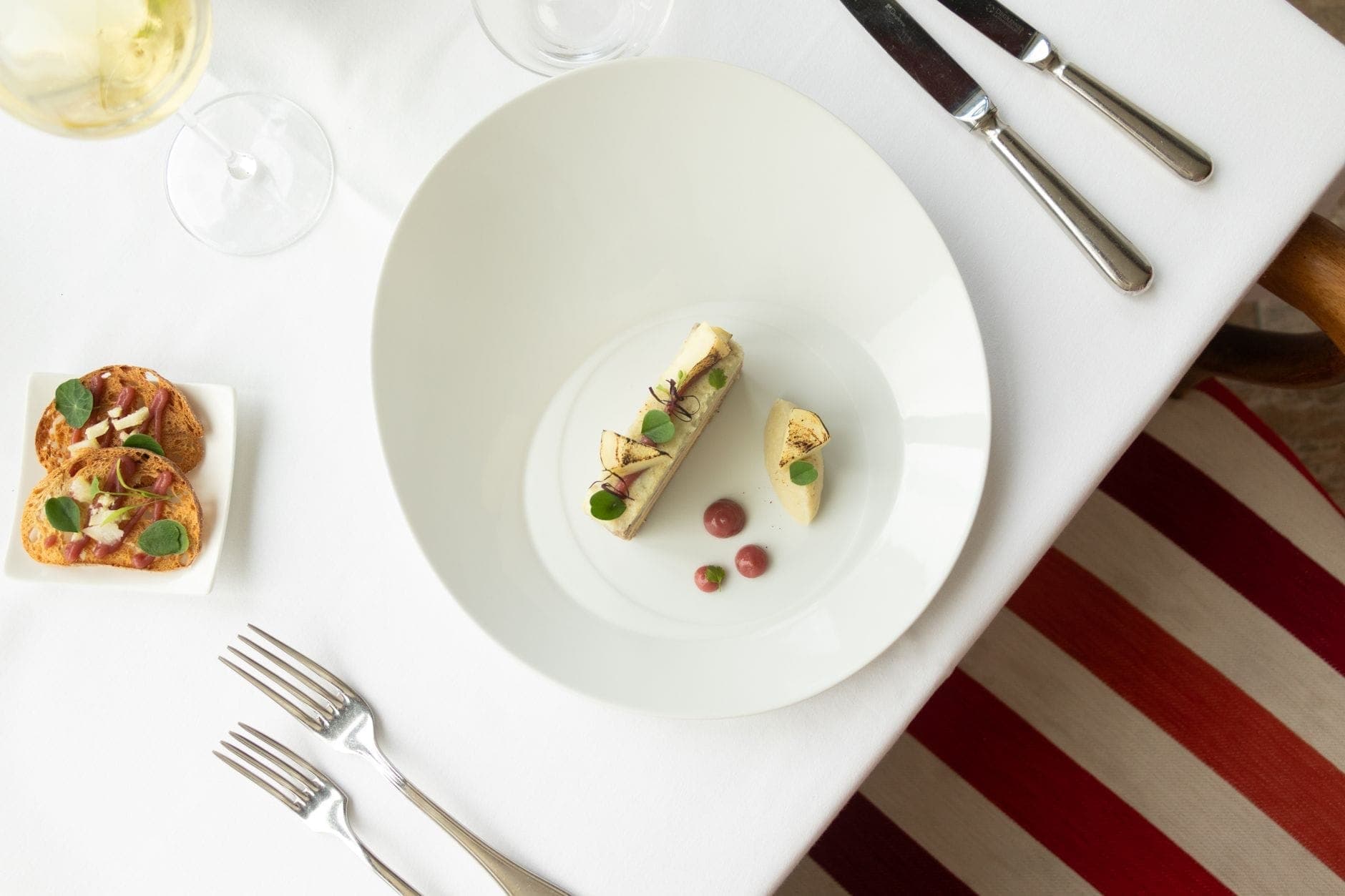 จานอาหารหรูและ amuse-bouches บนผ้าปูโต๊ะสีขาว พร้อมแก้วไวน์และช้อนส้อมมีดในร้านอาหาร fine dining