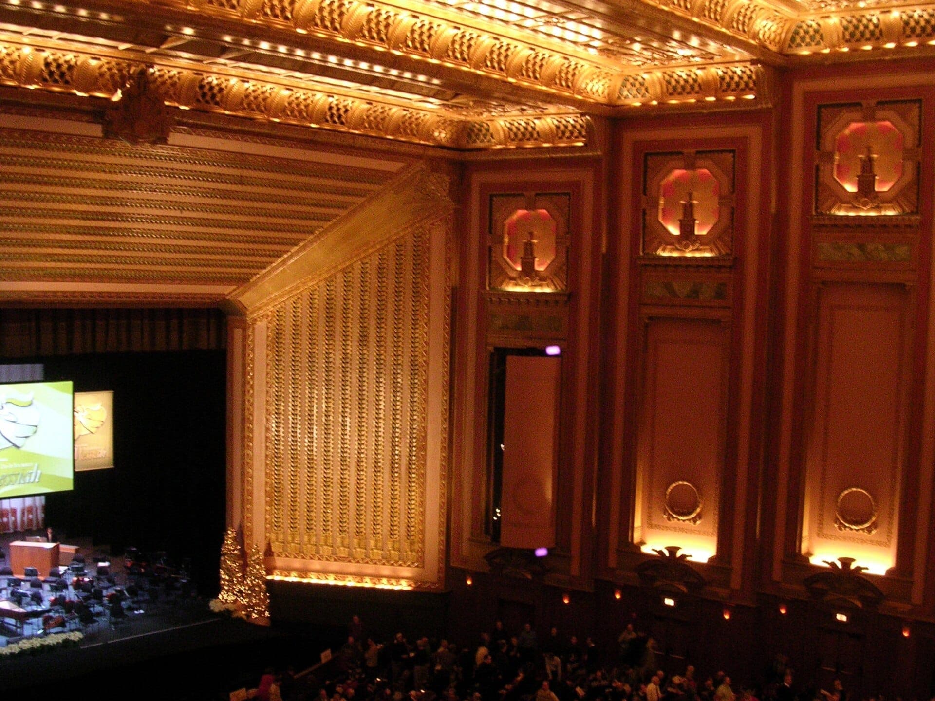 Prachtvolles Inneres der Lyric Opera of Chicago mit verzierten goldenen Wänden, Bühnenvorbereitung, dramatischer Beleuchtung und Zuschauern auf der Suche nach ihren Plätzen.