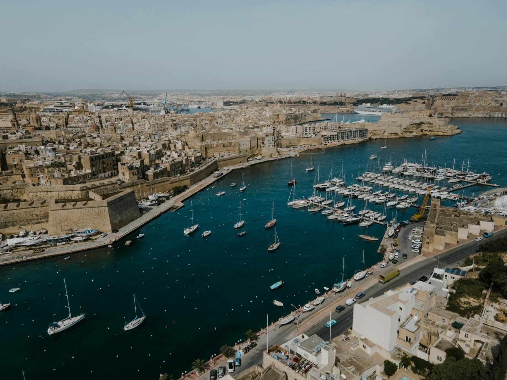 Vue aérienne du Grand Harbour à Malte montrant les fortifications historiques, la marina avec de nombreux yachts et les bâtiments dorés de la ville.