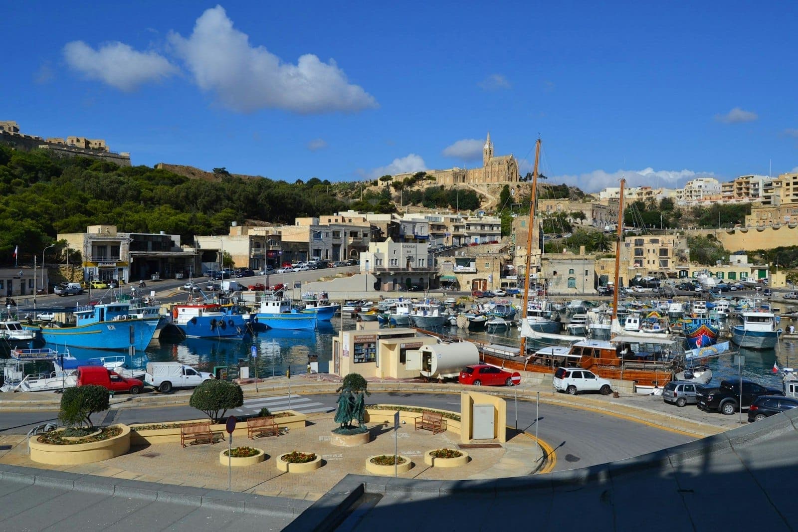 Vue ensoleillée du port de Mġarr à Gozo avec des bateaux amarrés dans la marina et la ville s'élevant sur la colline en arrière-plan.
