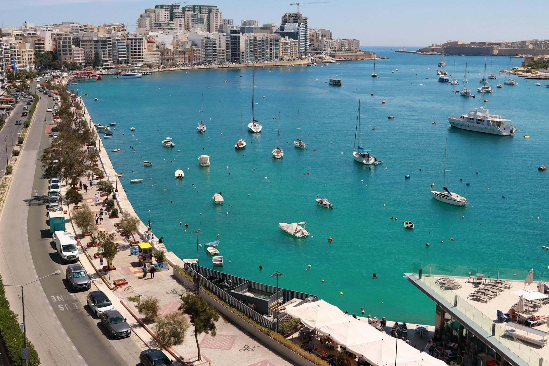 Luftaufnahme der Uferpromenade von Sliema auf Malta mit Booten in einer türkisfarbenen Bucht, modernen Gebäuden und einer belebten Küstenstraße – optimale Lage für die Tauchlogistik.